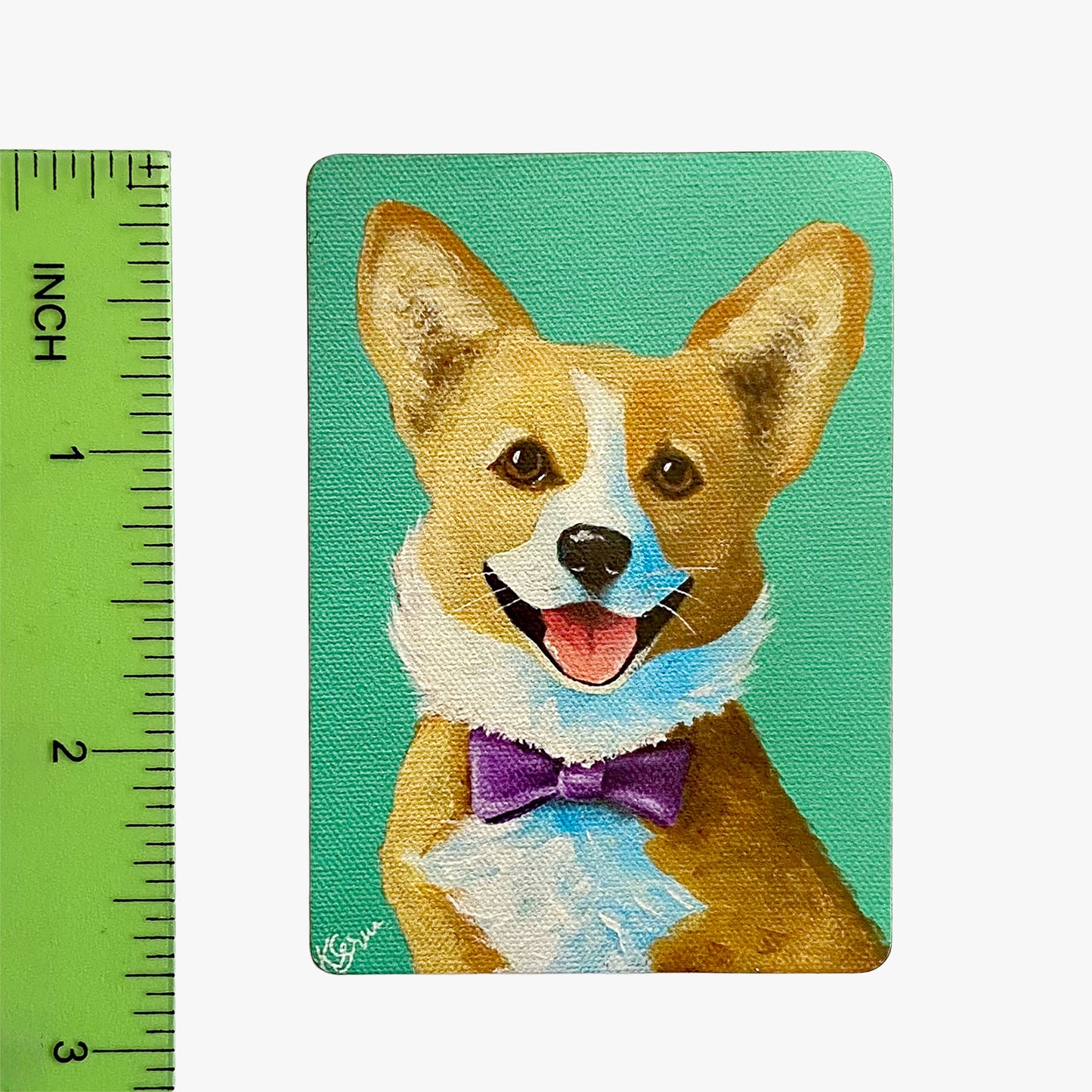 Magnet with a corgi dog wearing a purple bow tie on a teal background, next to a ruler for scale.