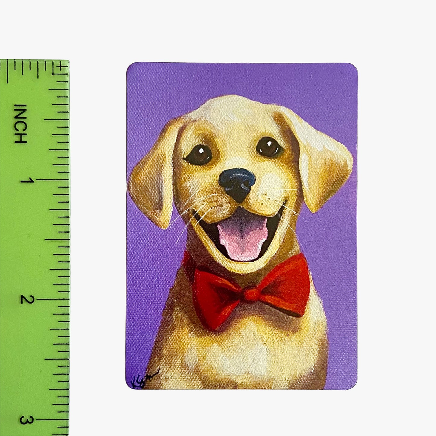 Magnet with a dog wearing a red bow tie on a purple background, next to a ruler for scale.