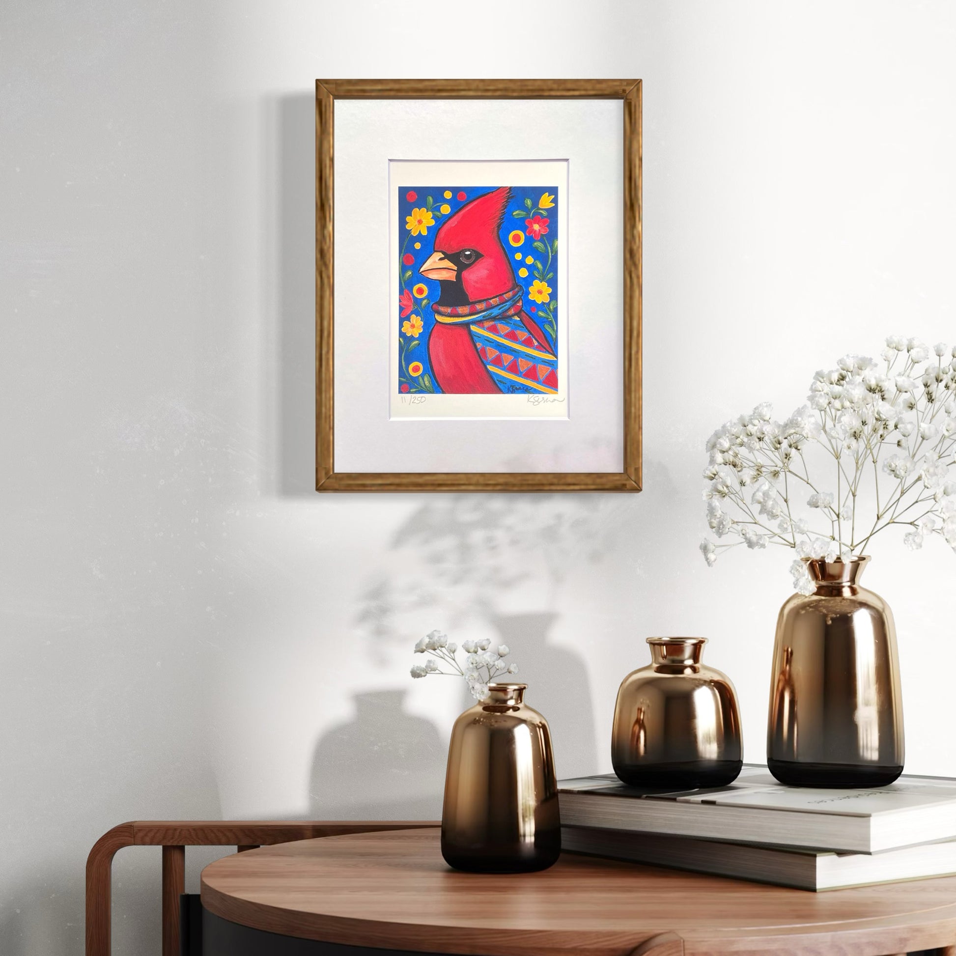 Framed artwork of a red bird with a blue background on a wall above a wooden table with decorative vases.