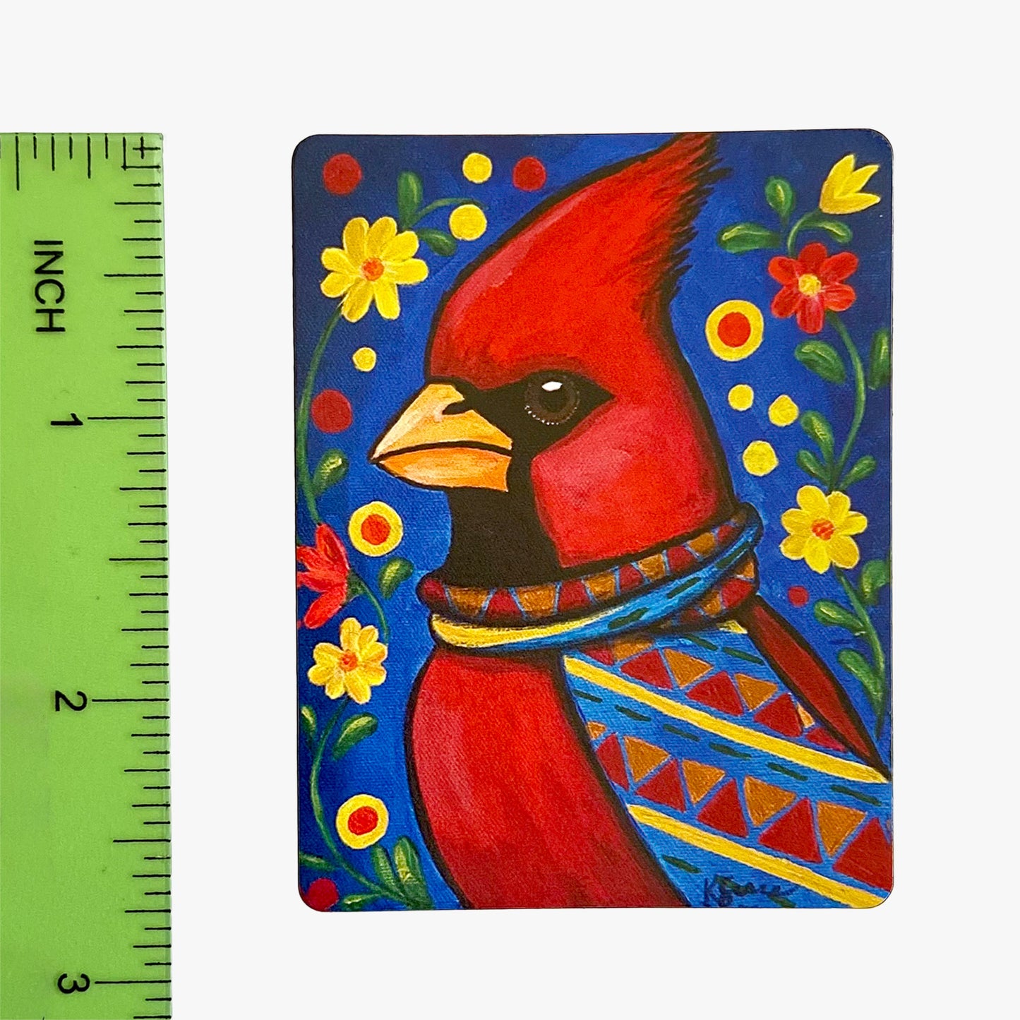 Painting of a red cardinal bird with a colorful patterned scarf on a blue background with flowers, next to a ruler for scale.
