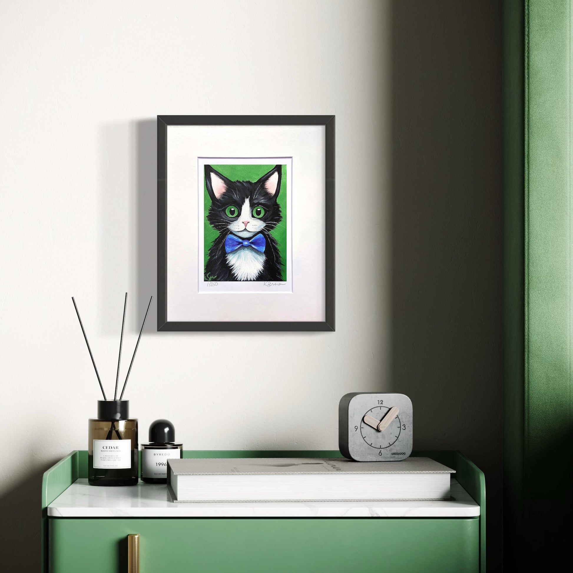 Framed artwork of a black and white cat with green eyes on a wall above a green cabinet.