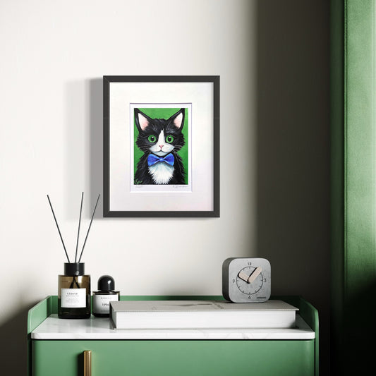 Framed artwork of a black and white cat with green eyes on a wall above a green cabinet.