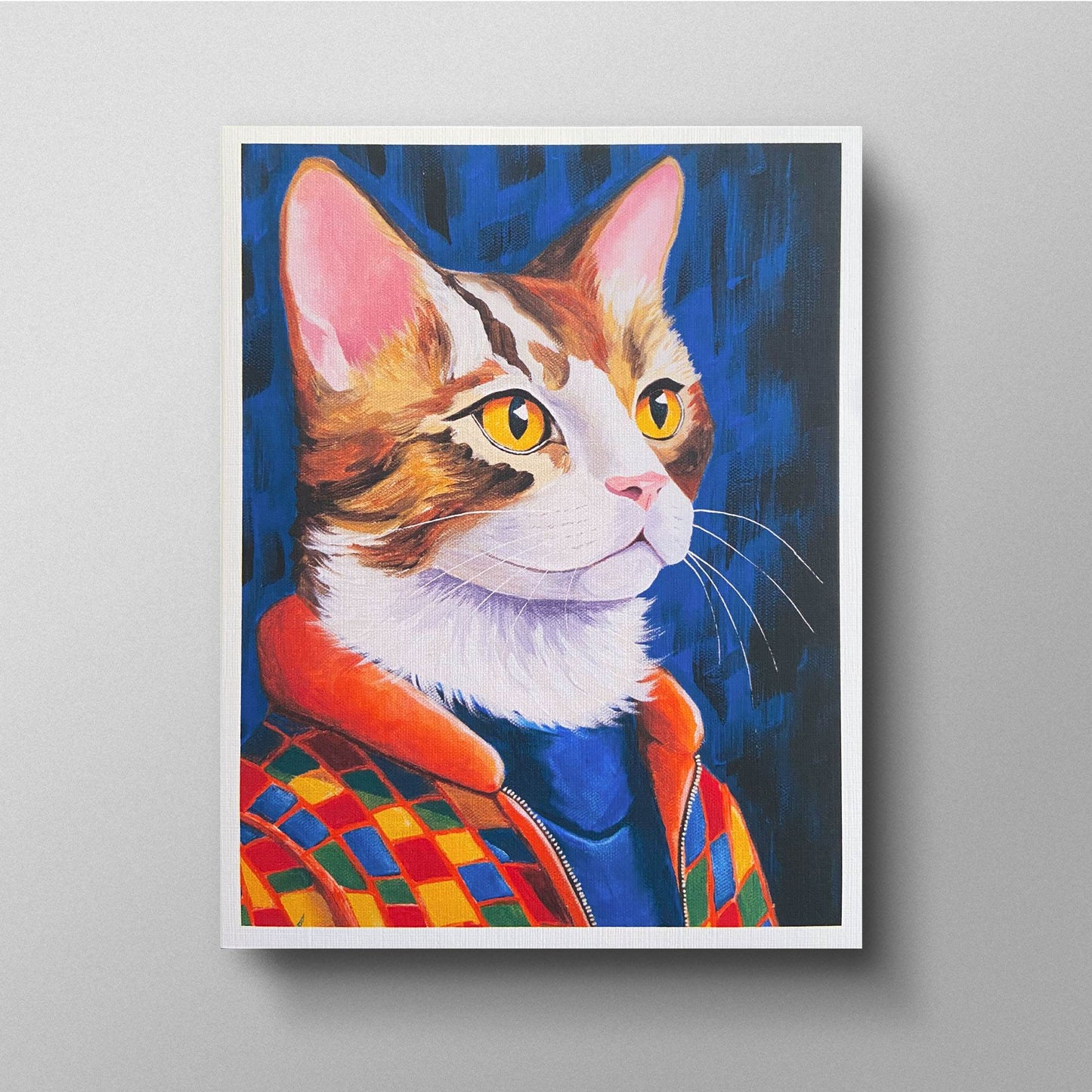 A colorful image of a cat named Jasper, depicted wearing a stylish checkered jacket with an orange collar over a blue turtleneck. Jasper has striking golden eyes and a confident expression, set against a deep blue background. The artwork is presented on a greeting card with a white border.