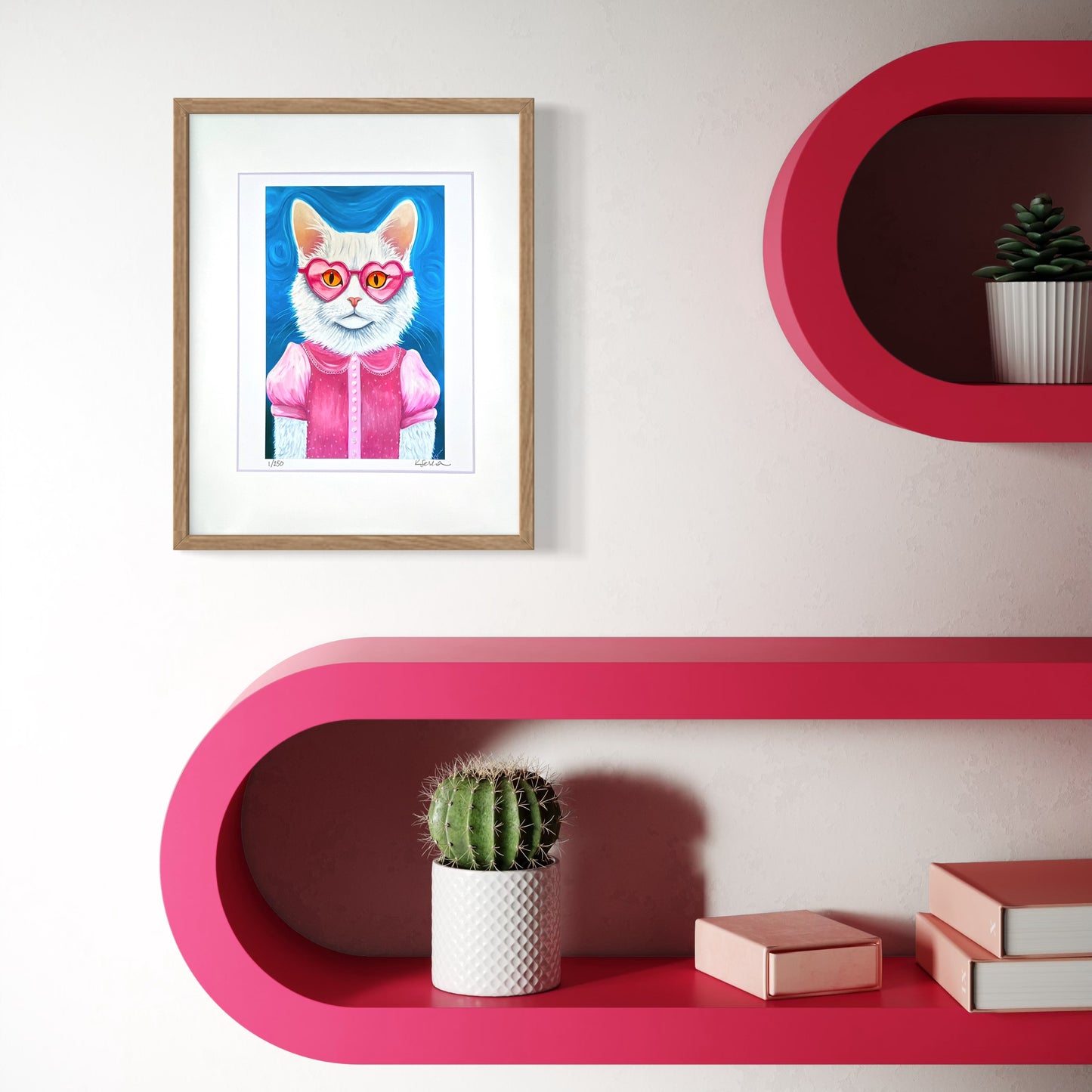A framed print of Lulu the Cat hangs on a light-colored wall, adding a whimsical and vintage-inspired charm. The natural wood frame and white mat make the pastel colors pop. Below, a bold pink shelf with rounded edges holds a small cactus plant, pink books, and decorative objects, creating a fun and playful aesthetic.