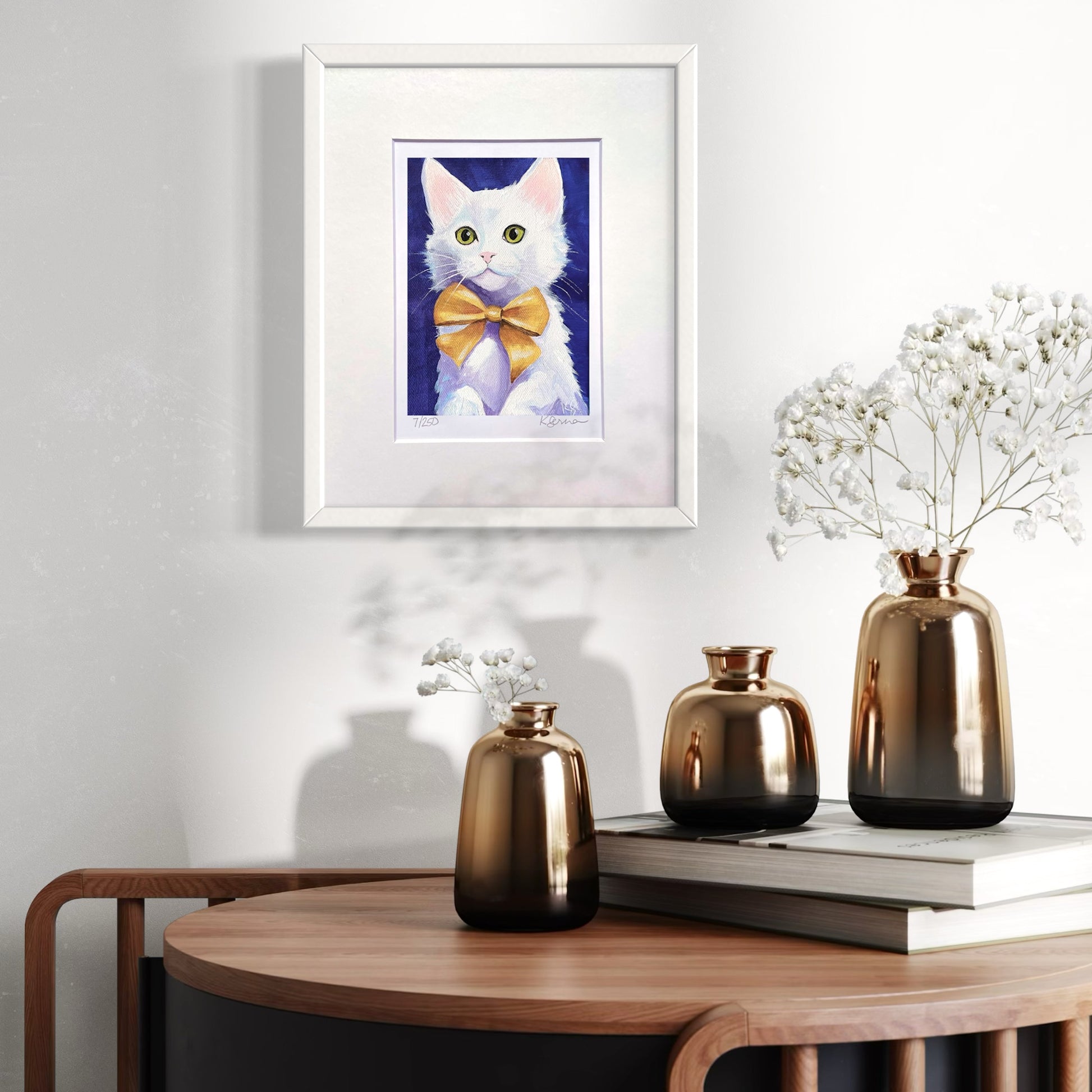 Framed artwork of a cat with a yellow bow tie on a wall above a wooden table with decorative vases.