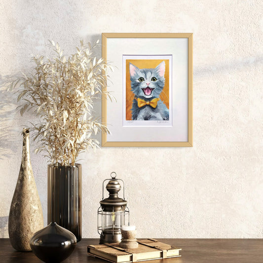Framed artwork of a cat with a yellow bow tie on a wall above decorative items.