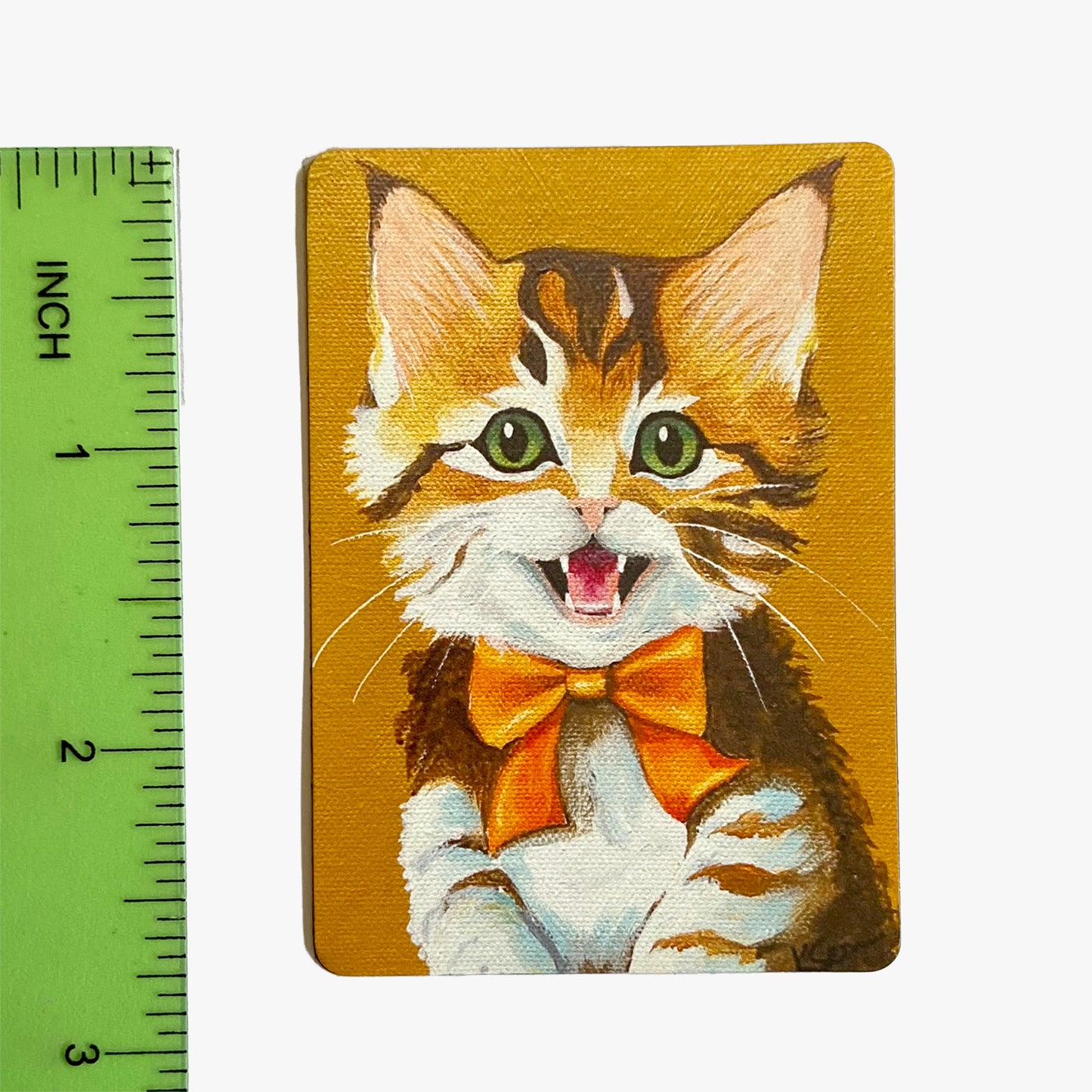 Magnet with a cat illustration wearing a bow tie next to a ruler for scale.