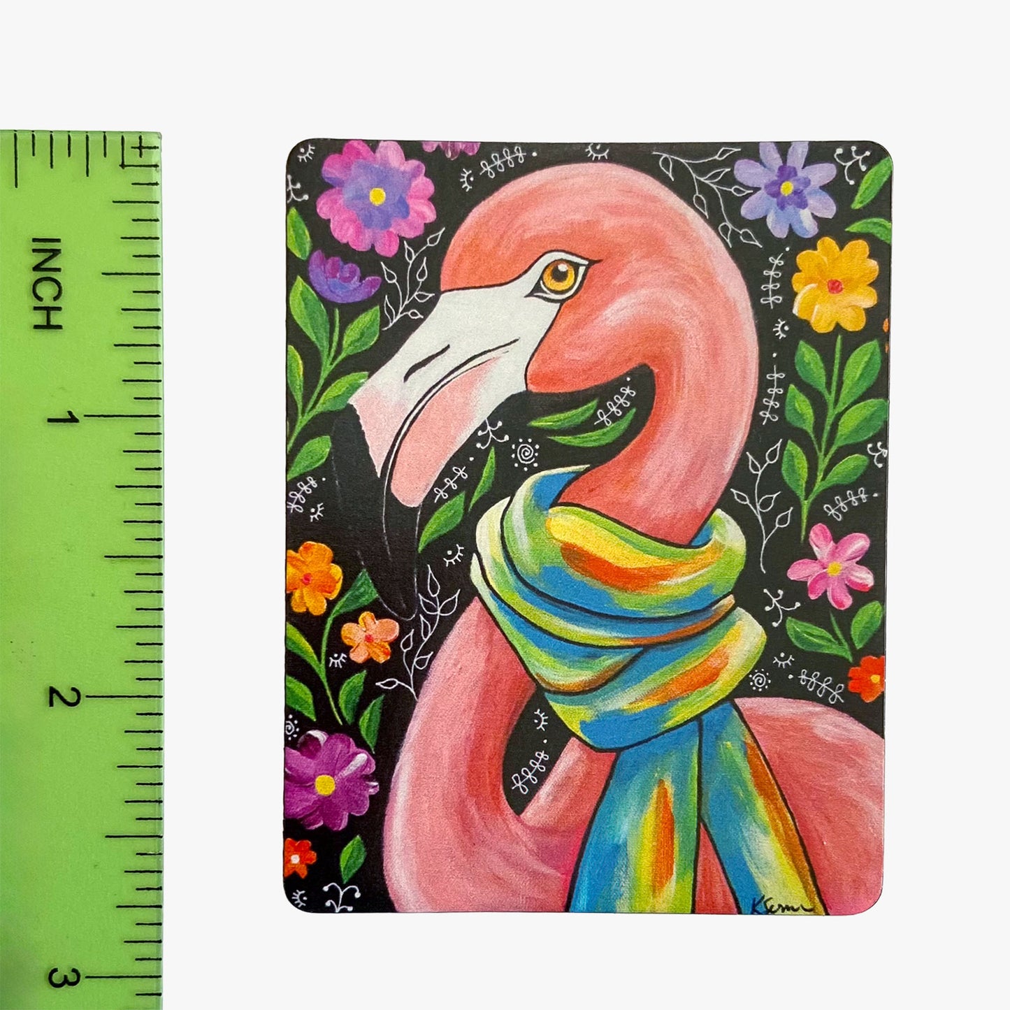 Colorful flamingo illustration with a scarf on a black background with flowers, next to a ruler for scale.