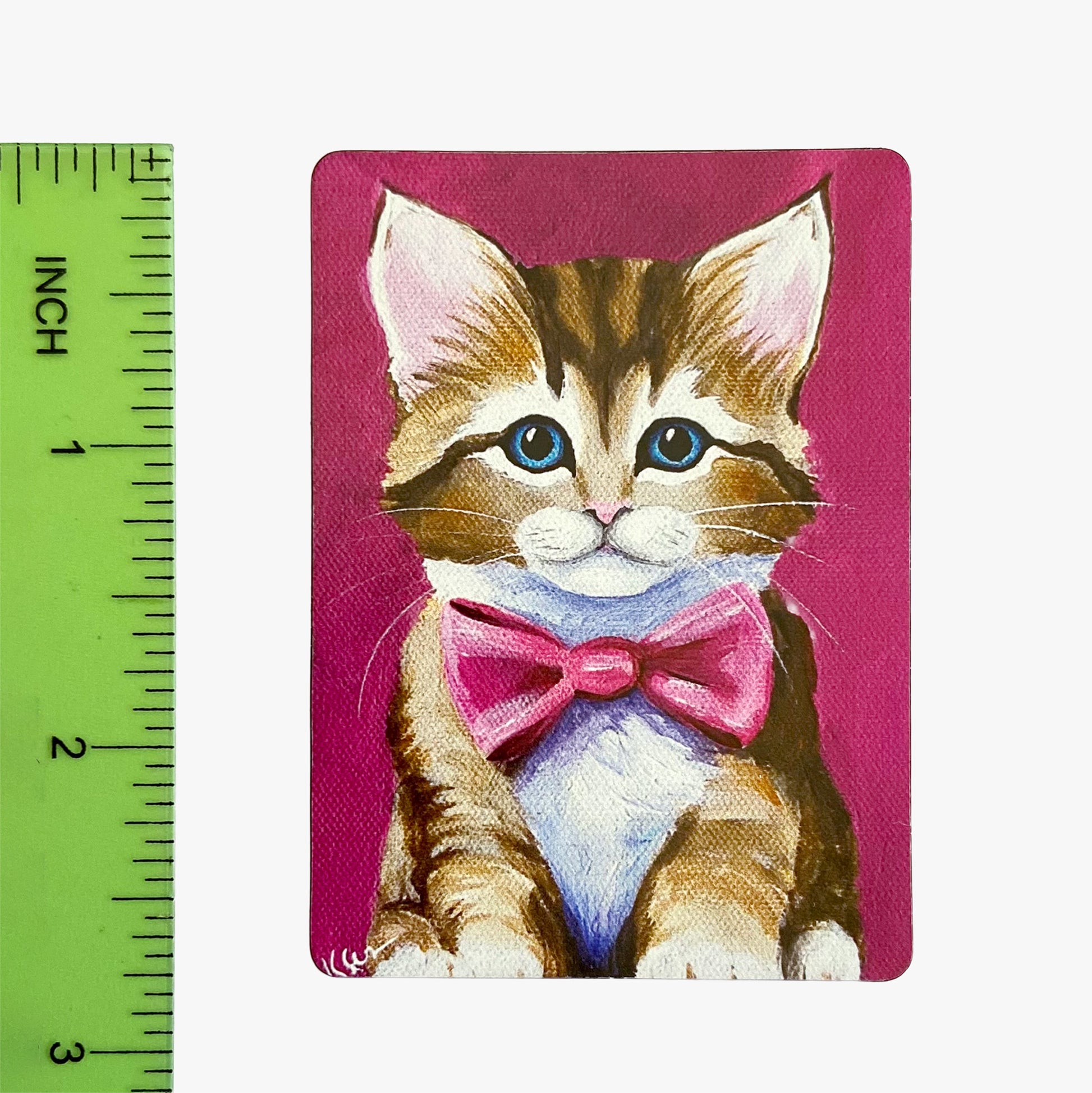 Magnet with a cat illustration wearing a pink bow tie on a pink background, next to a ruler for scale.