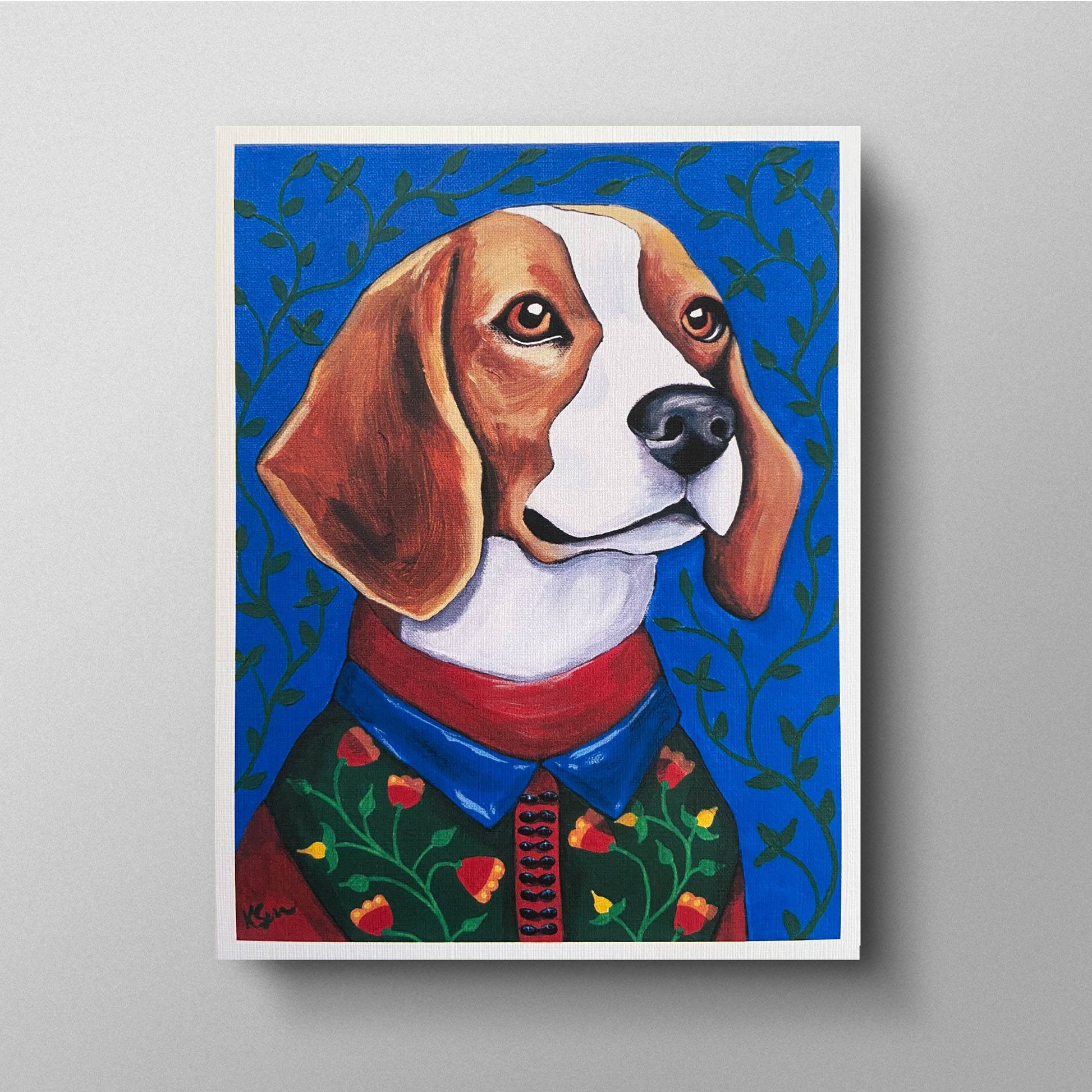 A colorful image of Theo the Beagle, a young and energetic dog with warm brown eyes. He is dressed in a green sweater adorned with small red and yellow flowers, layered over a red-collared blue shirt. The background is a vibrant blue with green vine-like patterns, adding to his lively and curious personality. The painting is presented on a greeting card with a white border.