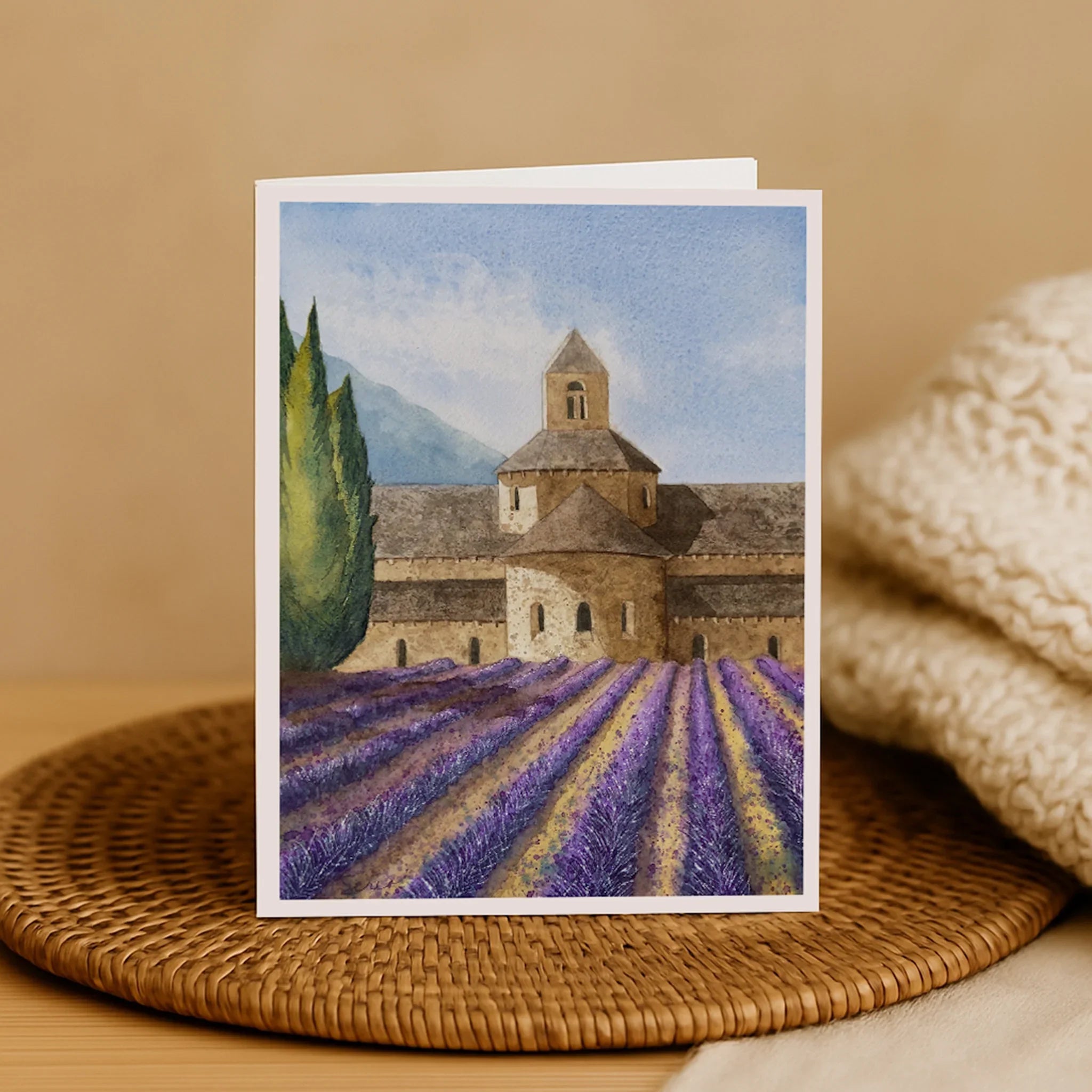 Greeting card with a lavender field and stone building design on a woven mat.