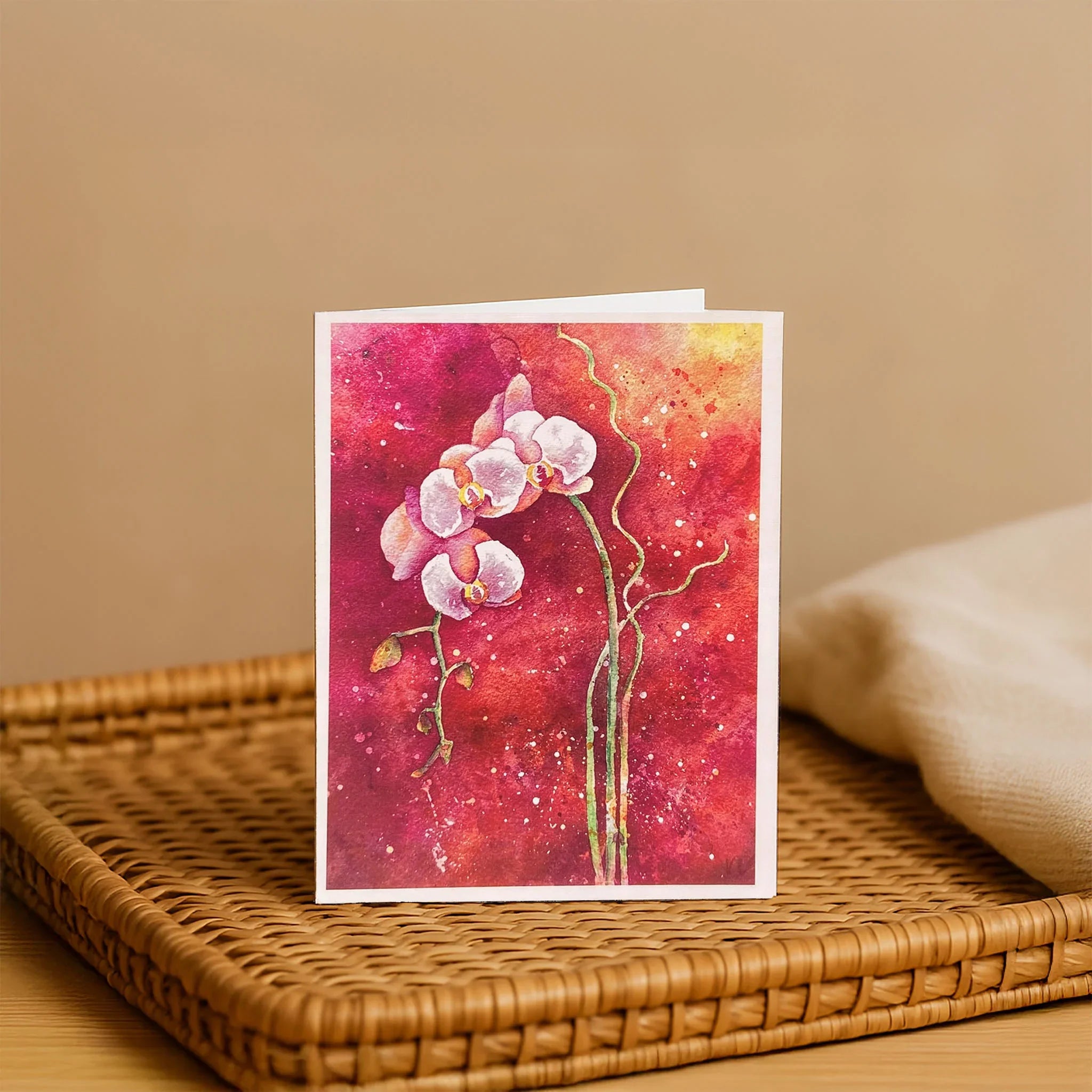 Greeting card with pink orchid design on a red background, placed on a woven surface.