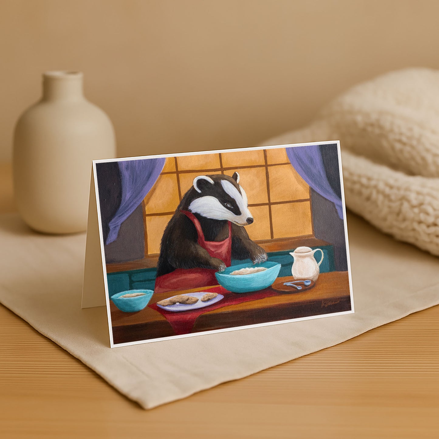 Greeting card with a badger character at a table on a beige surface.