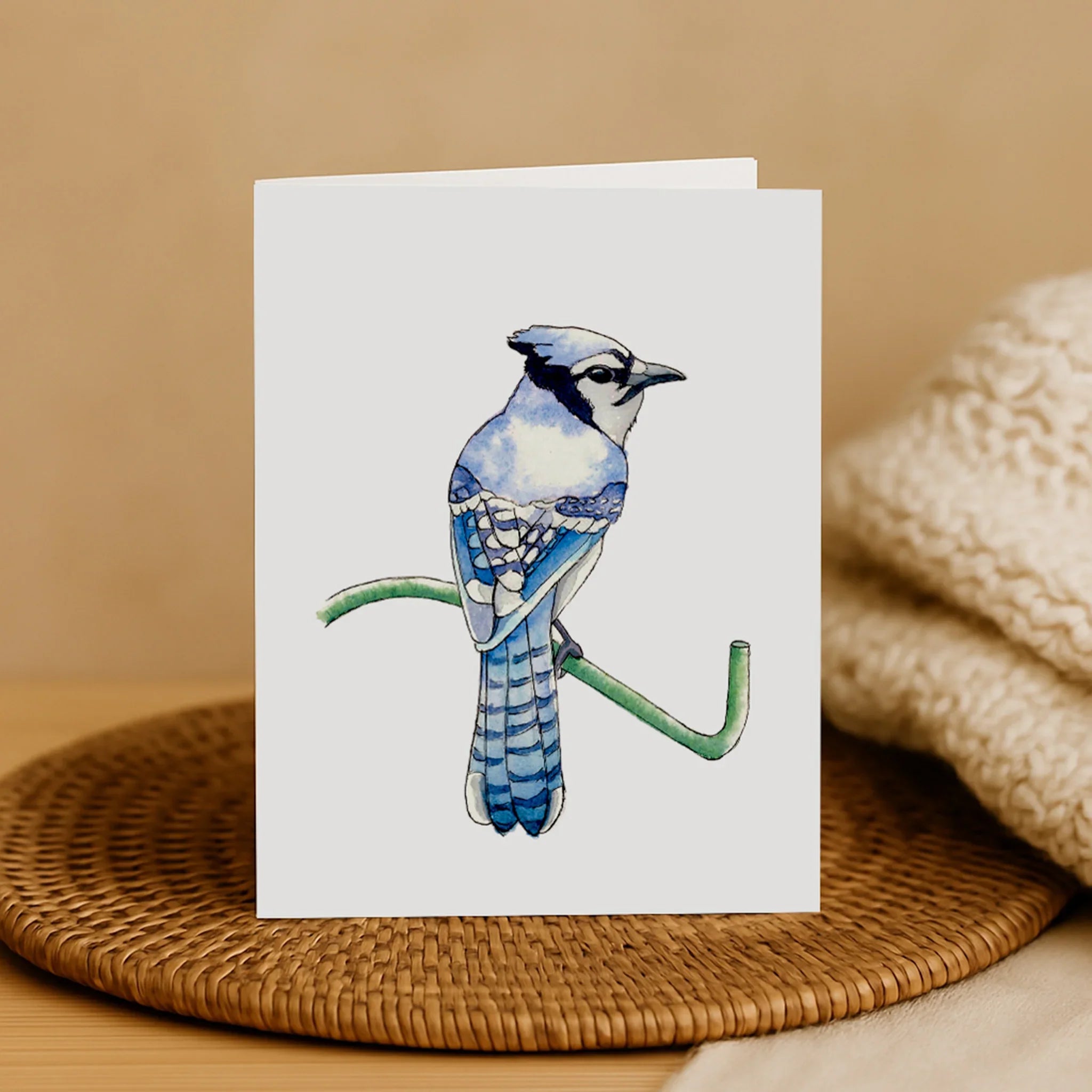 Greeting card with a blue jay illustration on a woven mat and beige background