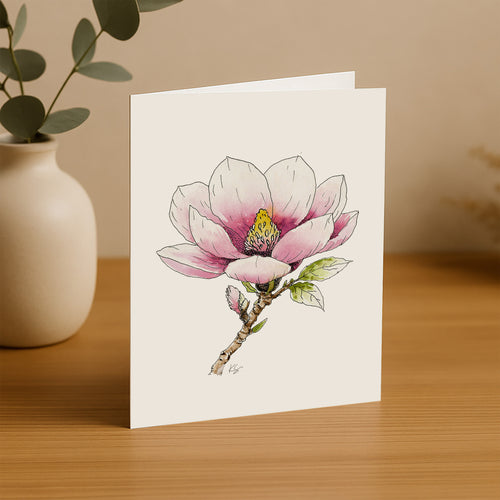Greeting card with a pink flower illustration on a wooden surface with a plant in the background