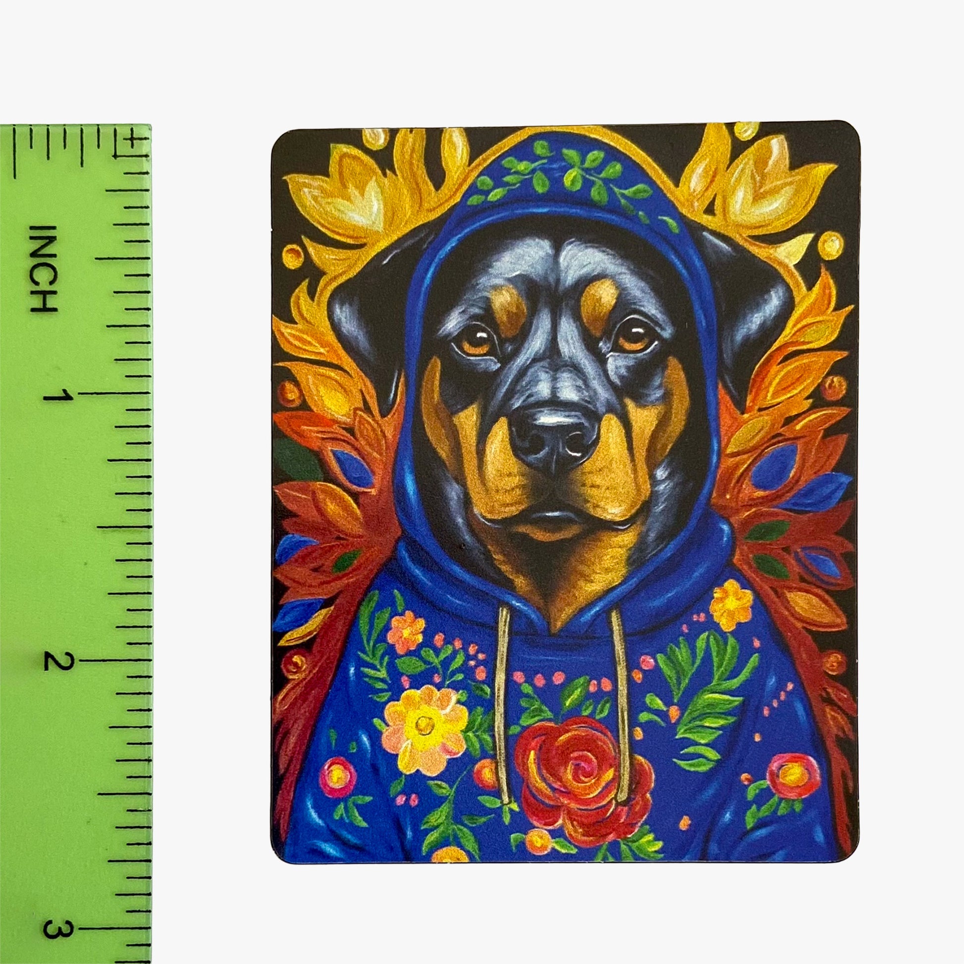 Colorful painting of a dog in a hoodie with floral elements next to a ruler for scale.