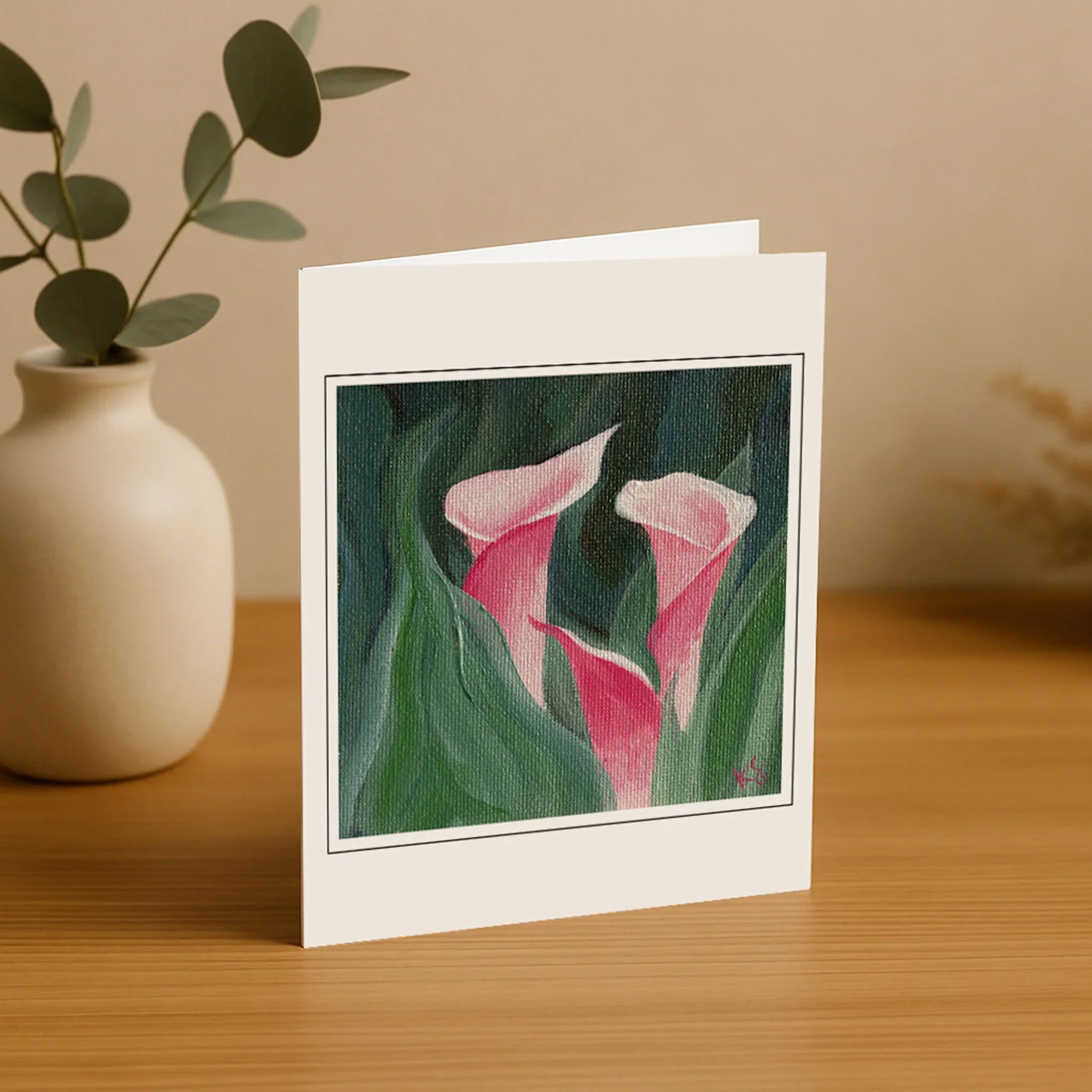 Greeting card with pink floral design on a wooden surface with a vase and plant.