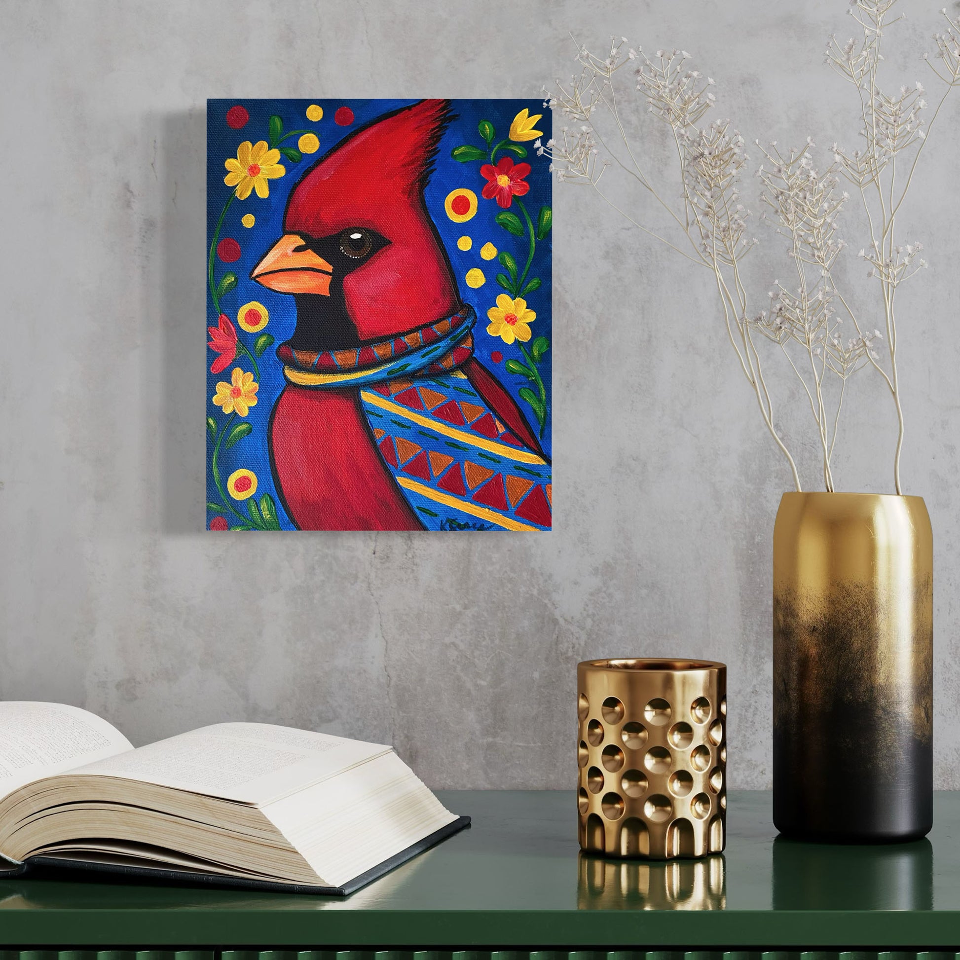 Painting of a red cardinal bird with flowers on a wall above a table with books and decorative items.