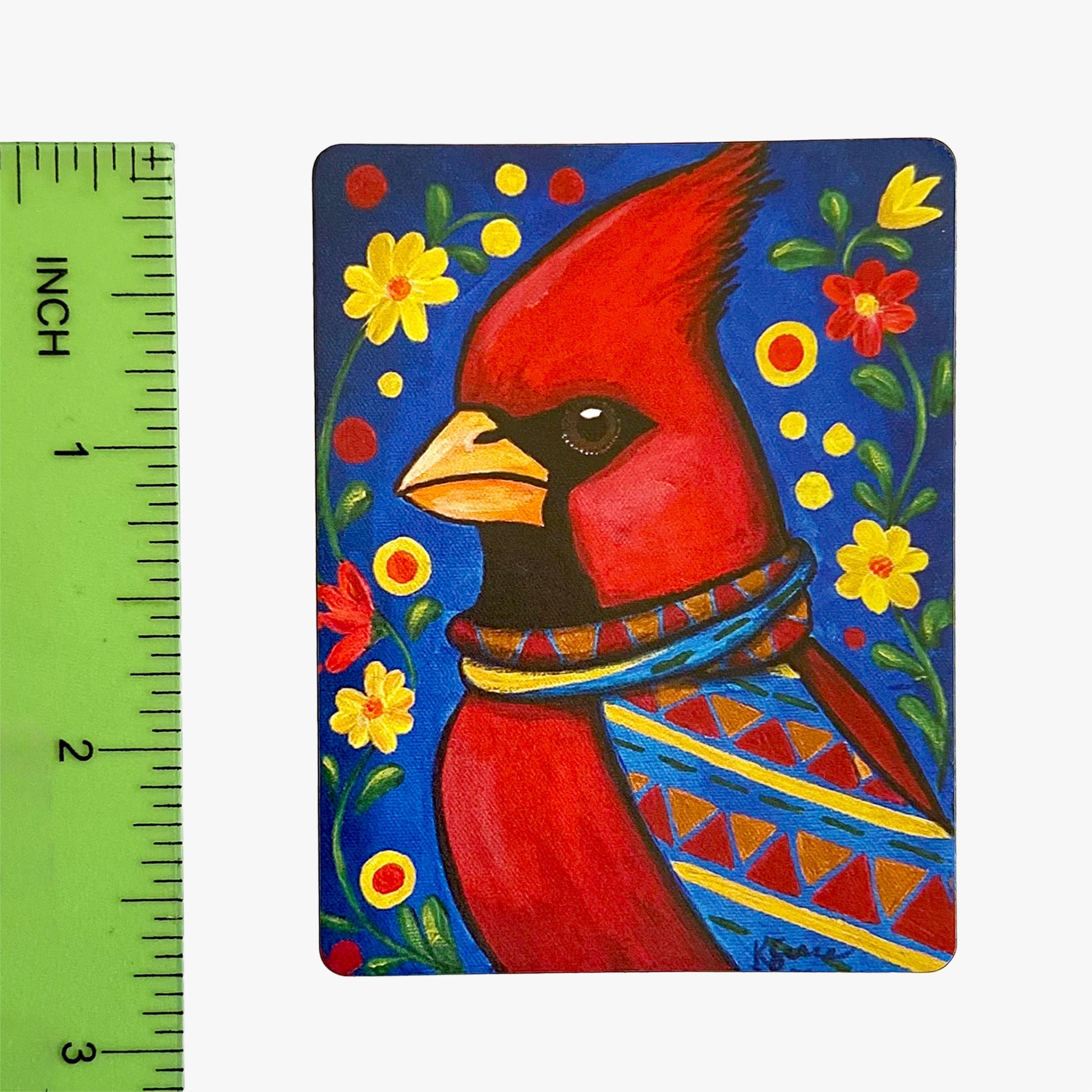Painting of a red cardinal bird with a colorful patterned scarf on a blue background with flowers, next to a ruler for scale.