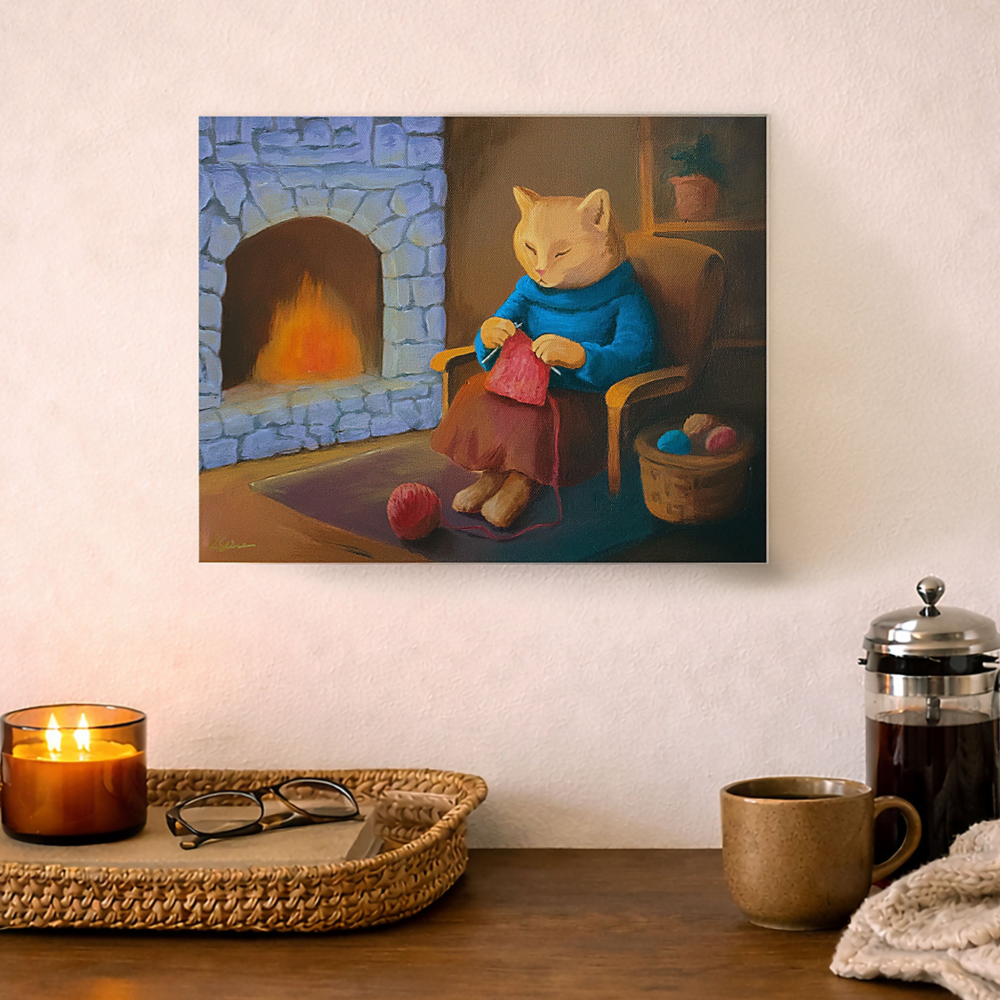 Painting of a cat in a cozy room with a fireplace, displayed on a wall above a table with a candle and mug.