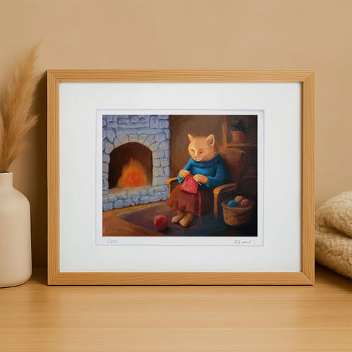 Framed artwork of a cat knitting by a fireplace on a wooden surface.