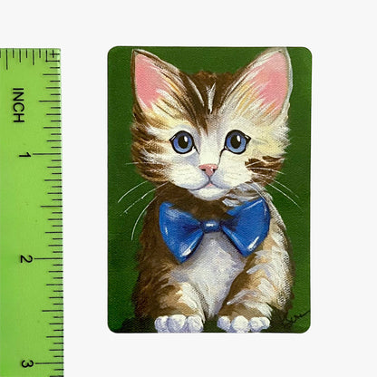 Illustration of a kitten with a blue bow tie on a green background with a ruler for scale.
