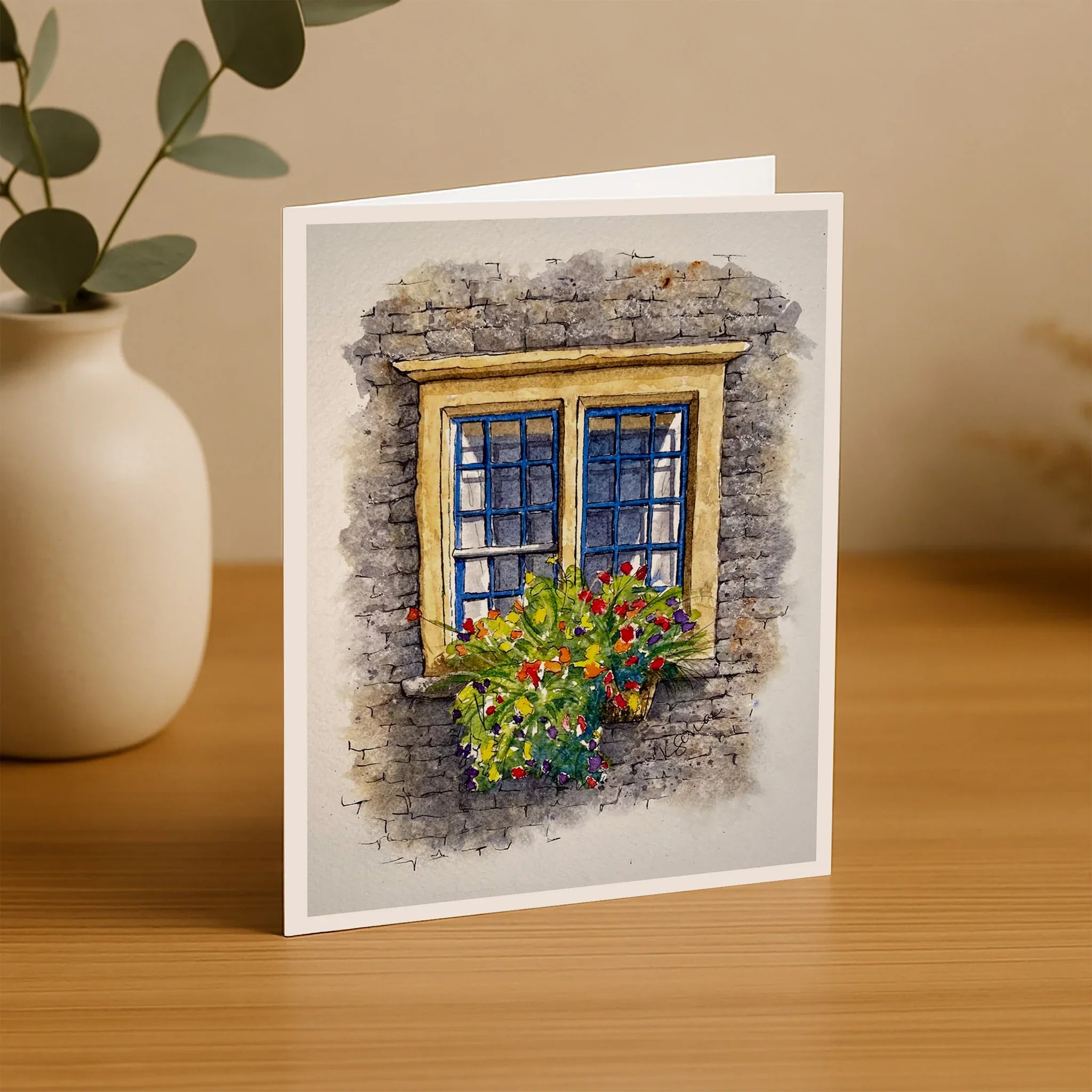 Greeting card with a stone window and flower box on a wooden surface with a plant.