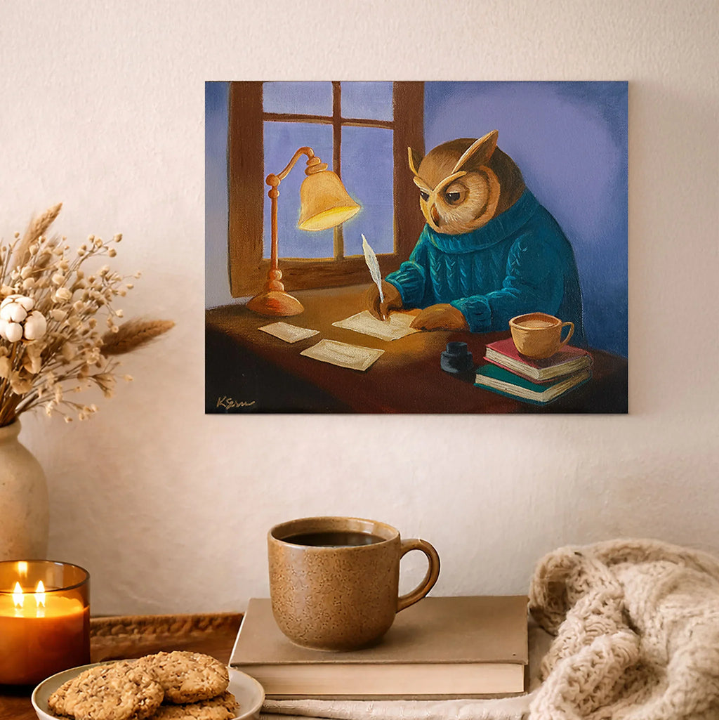 Painting of an owl in a blue robe writing at a desk with a lamp and books, displayed on a wall above a cozy setup with a mug, cookies, and candle.