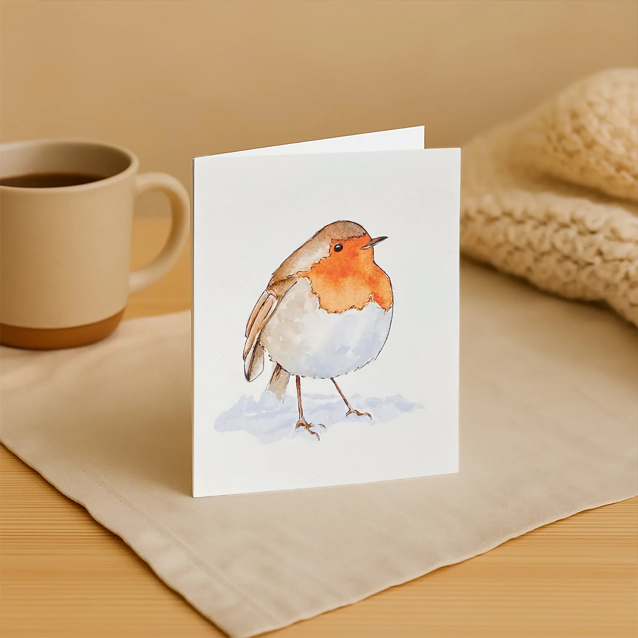 Card with a robin design on a table with a mug and fabric