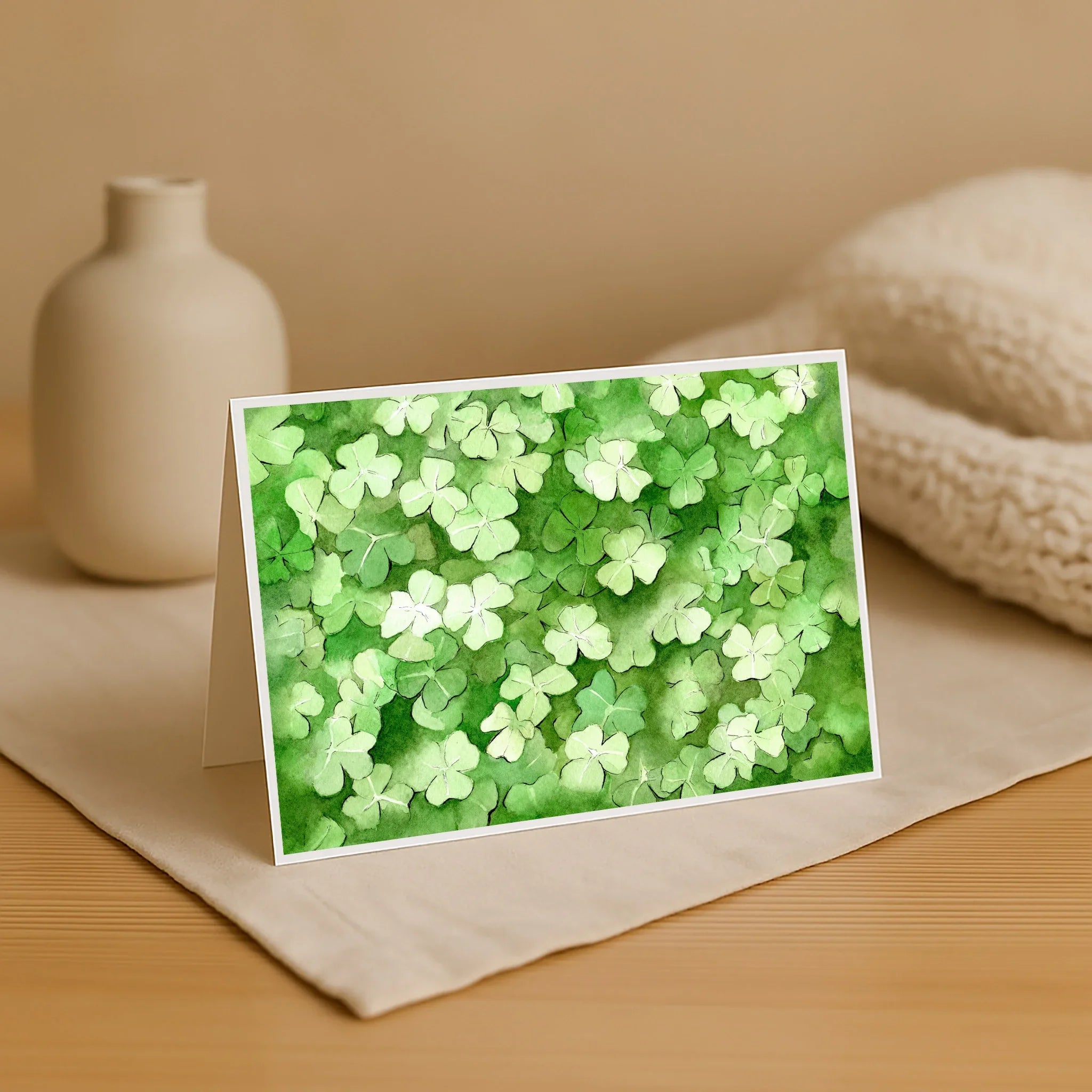 Card with green shamrock pattern on a beige surface with a vase and fabric.
