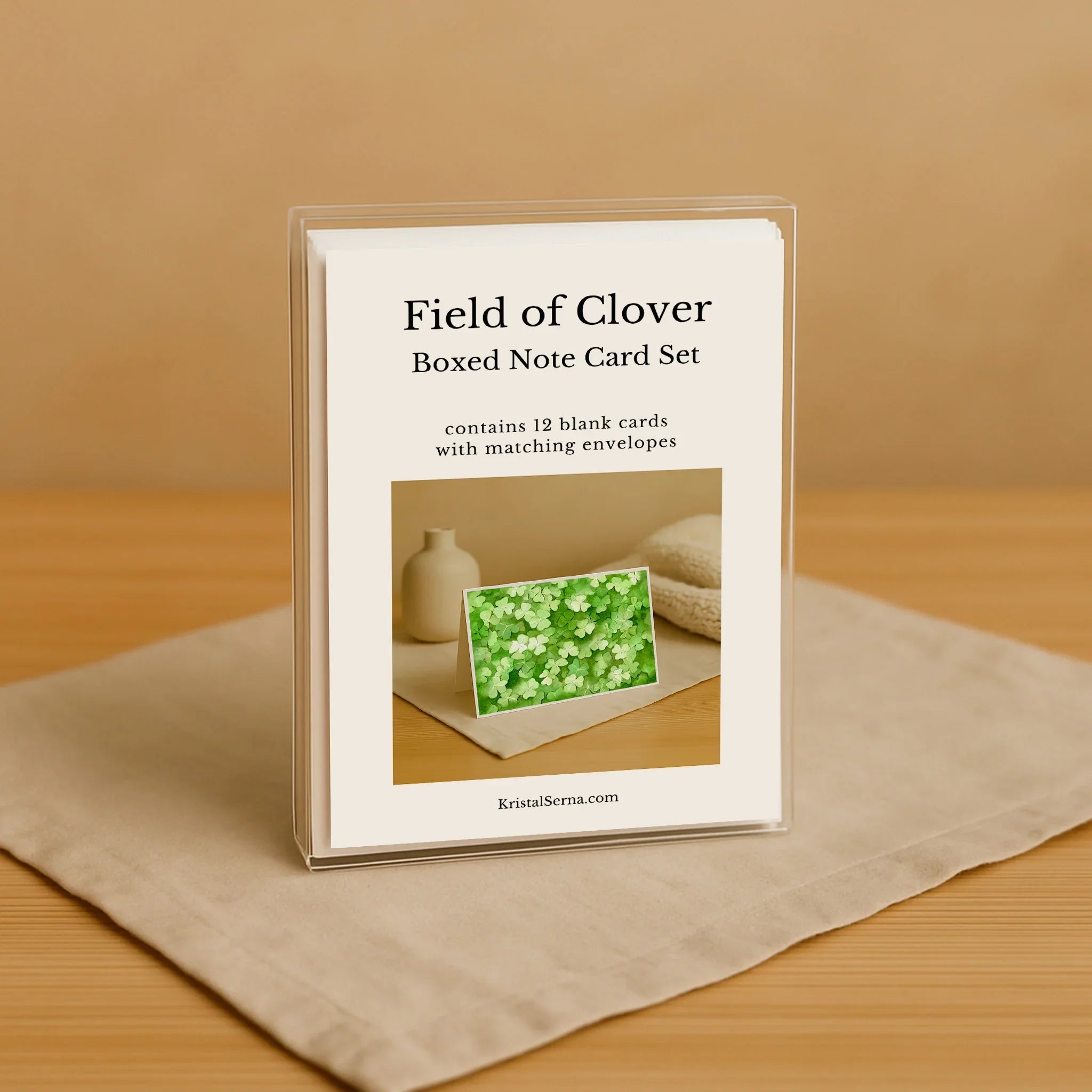 Boxed note card set titled 'Field of Clover' on a beige surface with a wooden background.