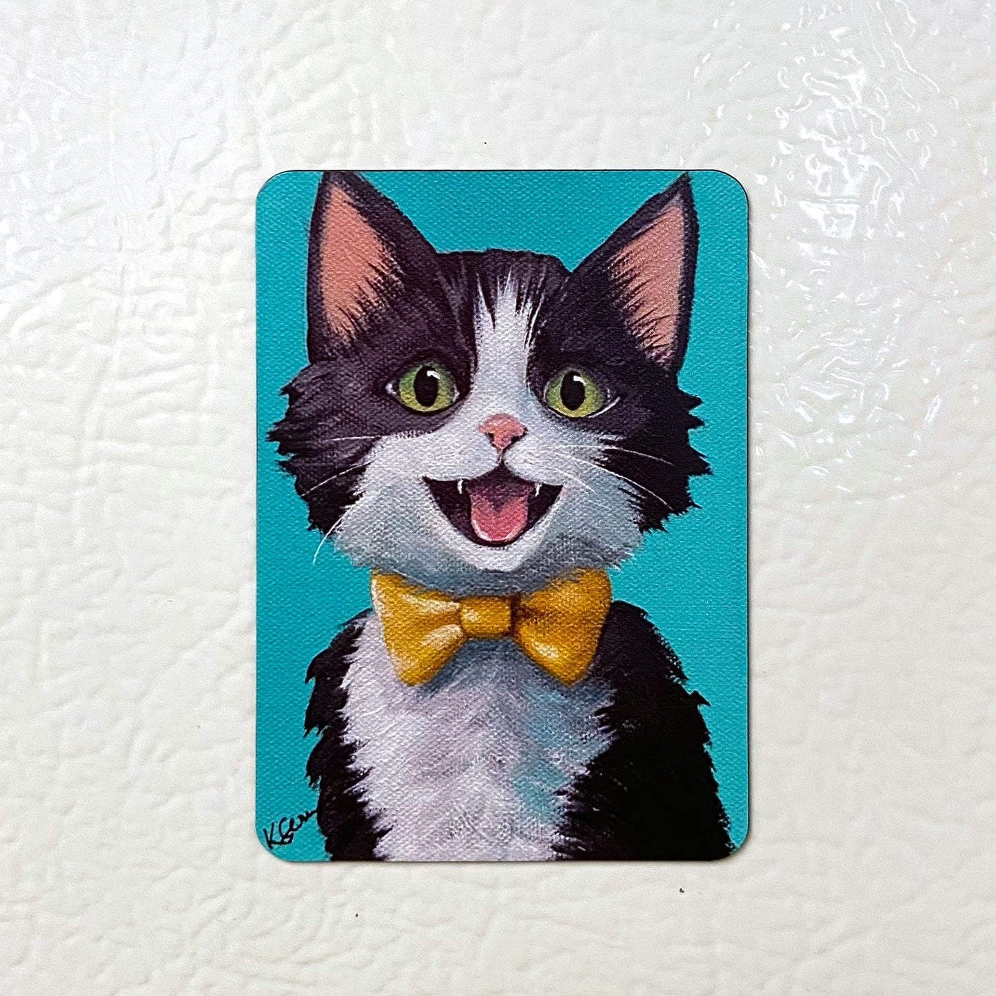Fridge magnet with a cartoon cat wearing a yellow bow tie on a white background