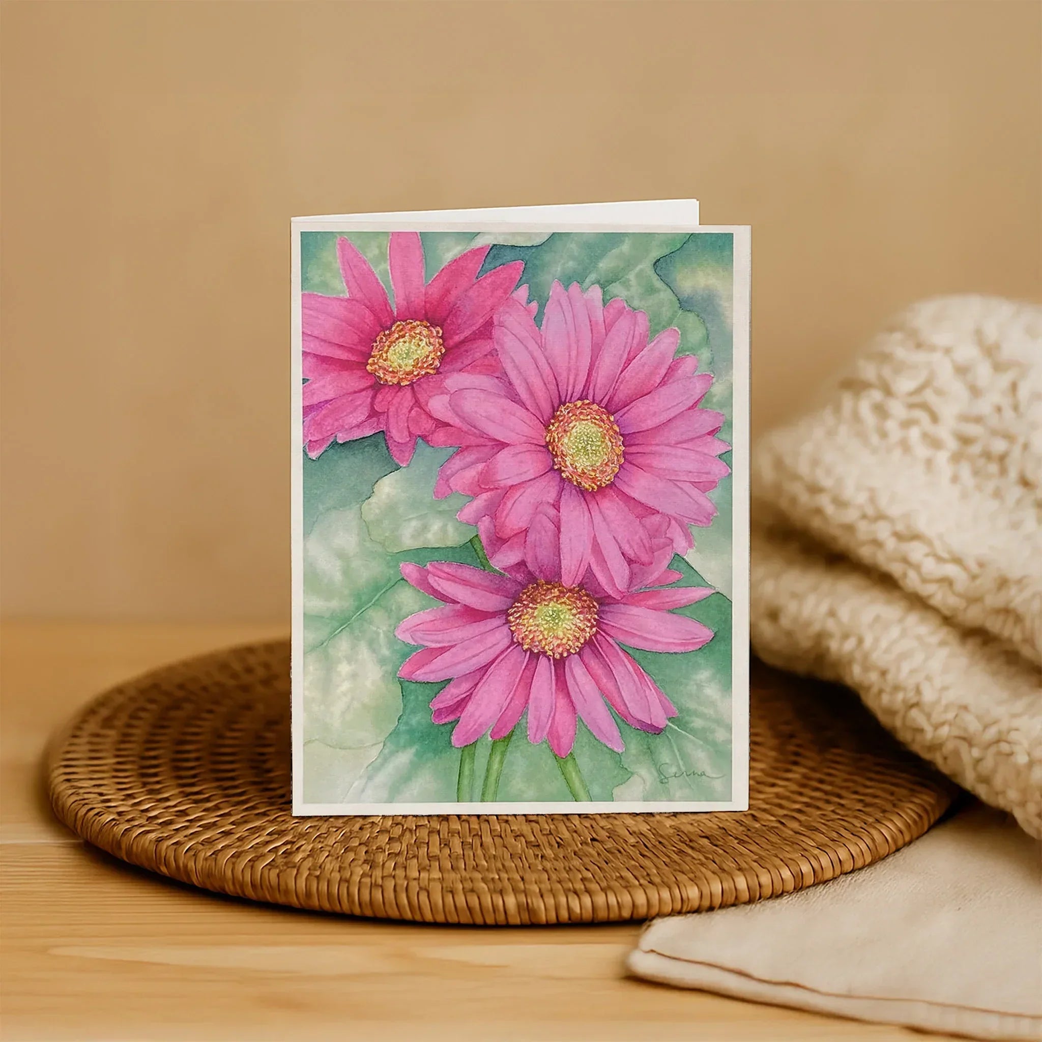 Card with pink flowers on a woven mat and beige fabric background