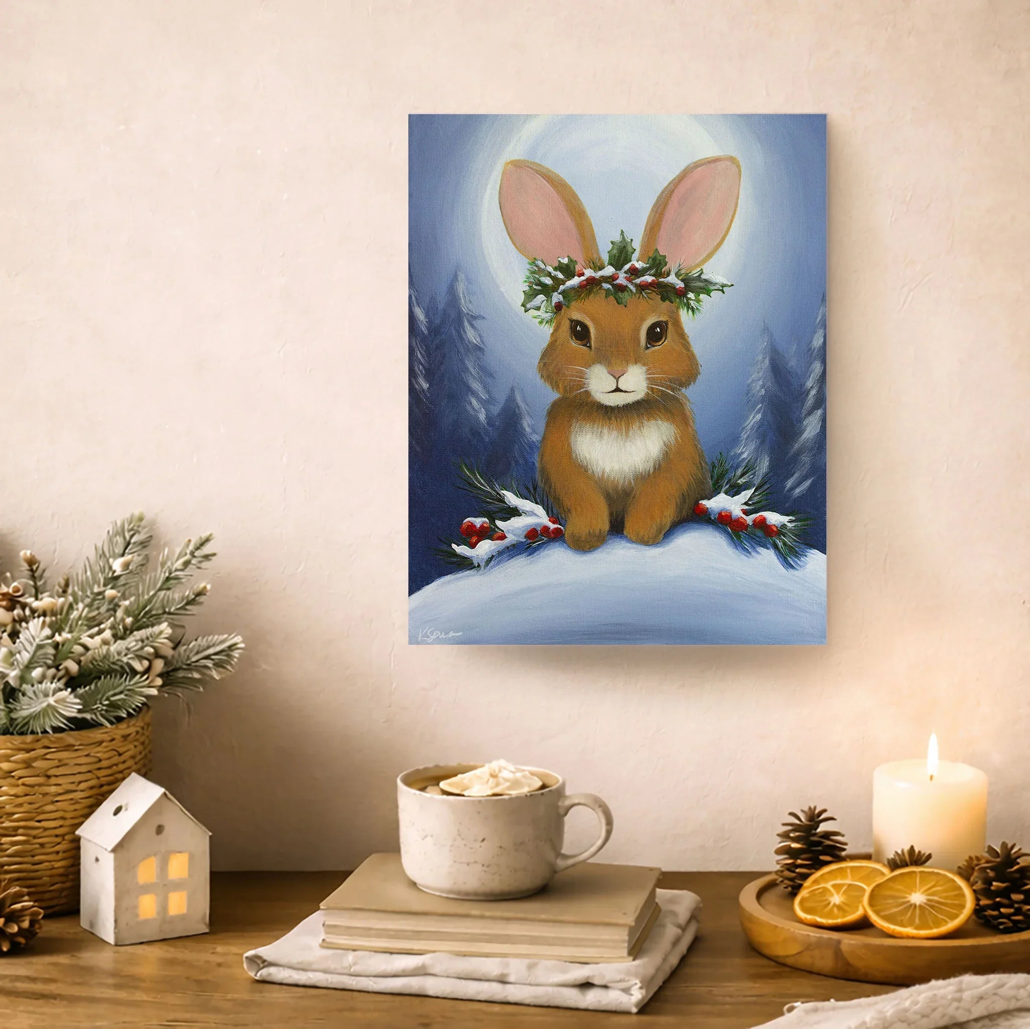Painting of a rabbit with a wreath on a wall above a table with a mug, books, and decorative items.