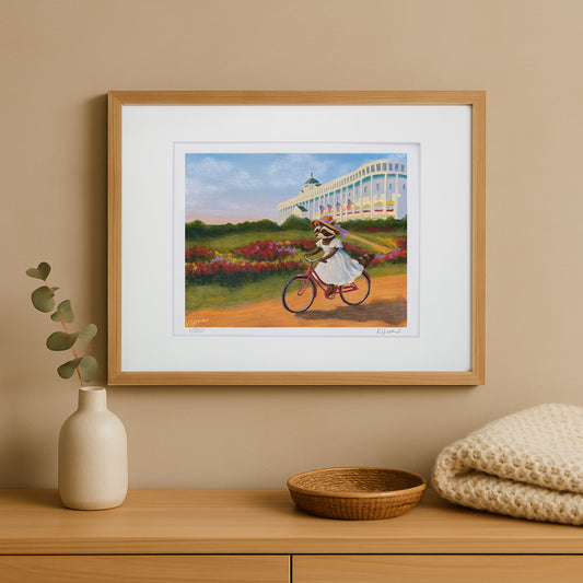 Framed artwork of a raccoon on a bicycle in a garden setting, displayed on a wooden shelf with decorative items.