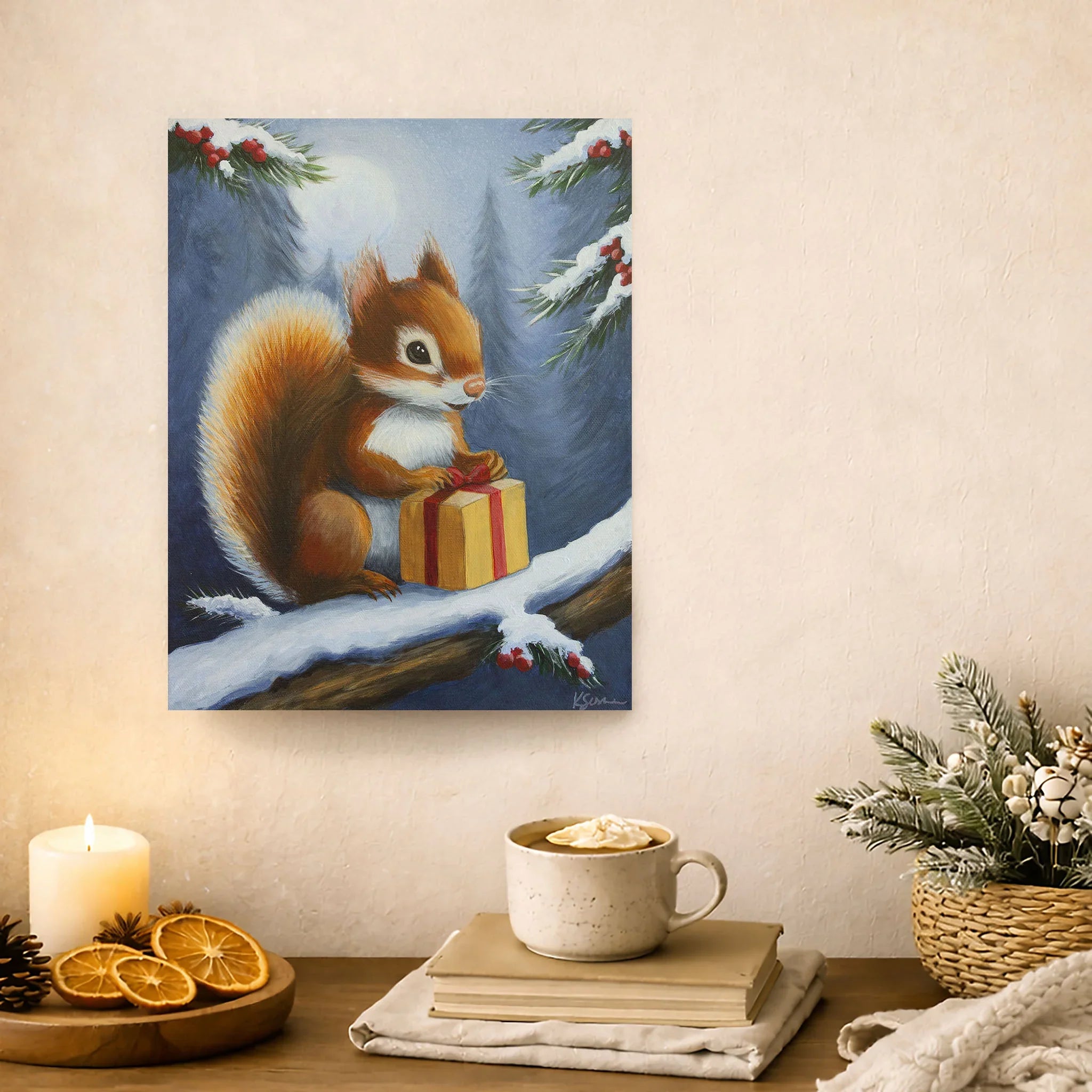 Painting of a squirrel with a gift on a snowy branch, displayed above a cozy setup with a mug, books, and decor.
