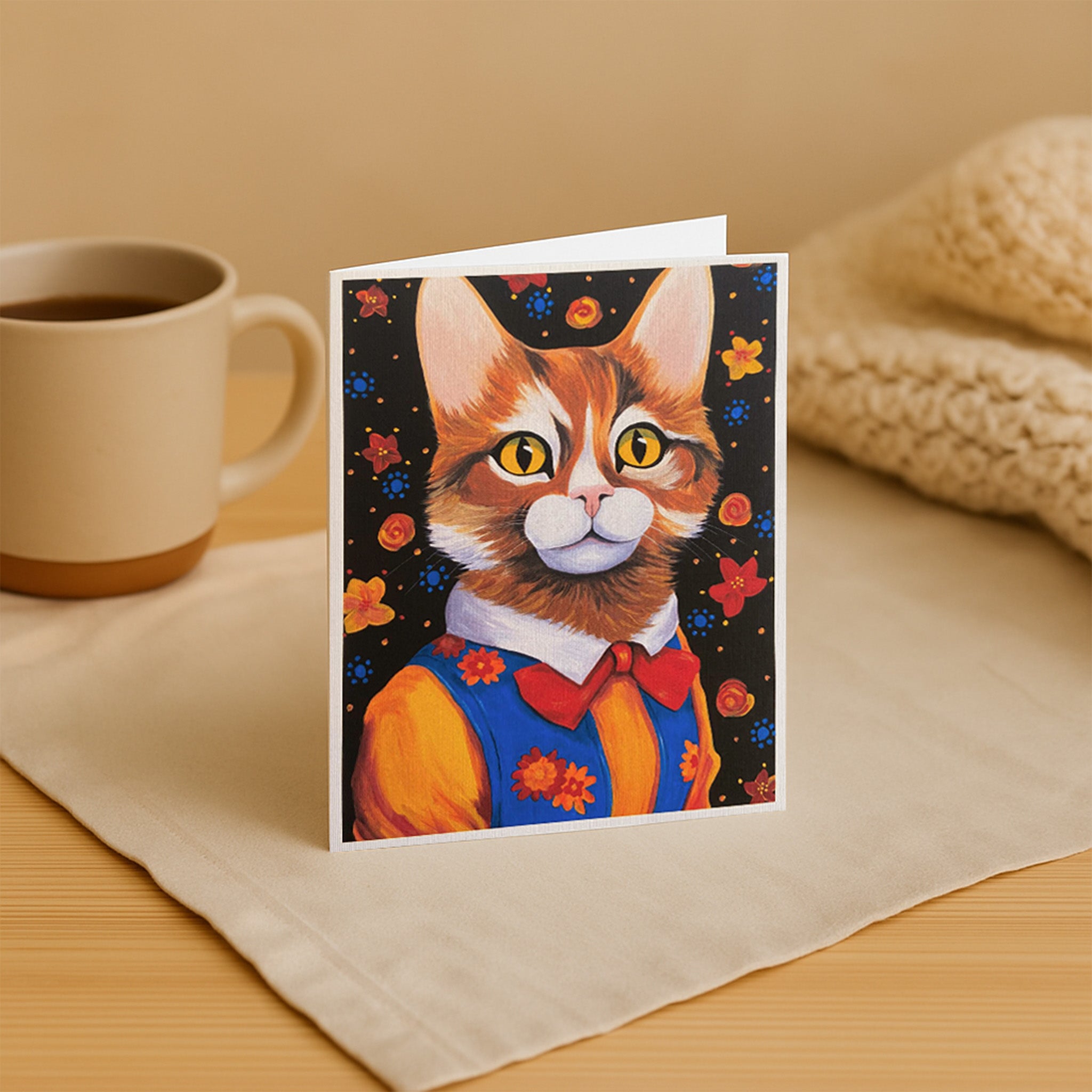 Greeting card with a cat illustration on a table with a mug and fabric.