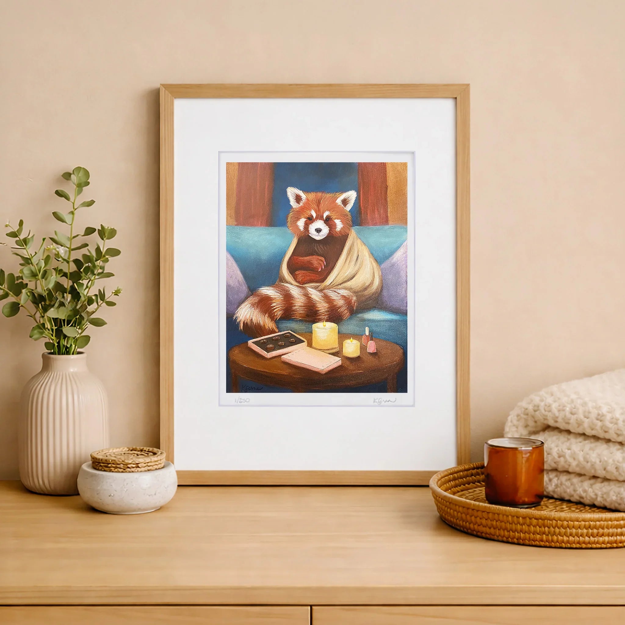 Framed artwork of a red panda on a sofa with a table holding chocolates, candles, and nail polish bottles.