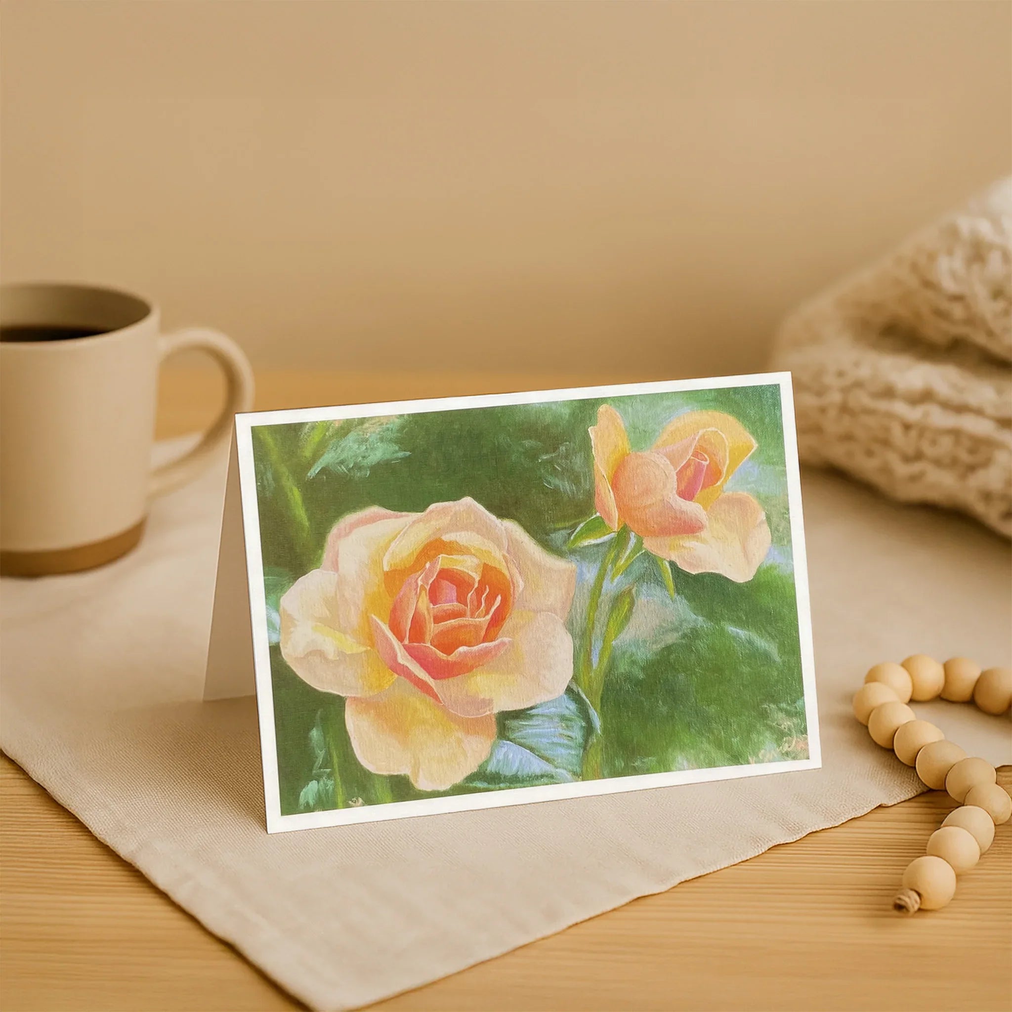 Card with a floral design on a wooden surface with a mug and beads.