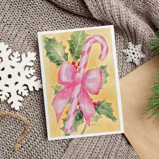 A watercolor and ink painting of a pink candy cane tied with a large pink bow, surrounded by green holly leaves and red berries on a warm golden background.