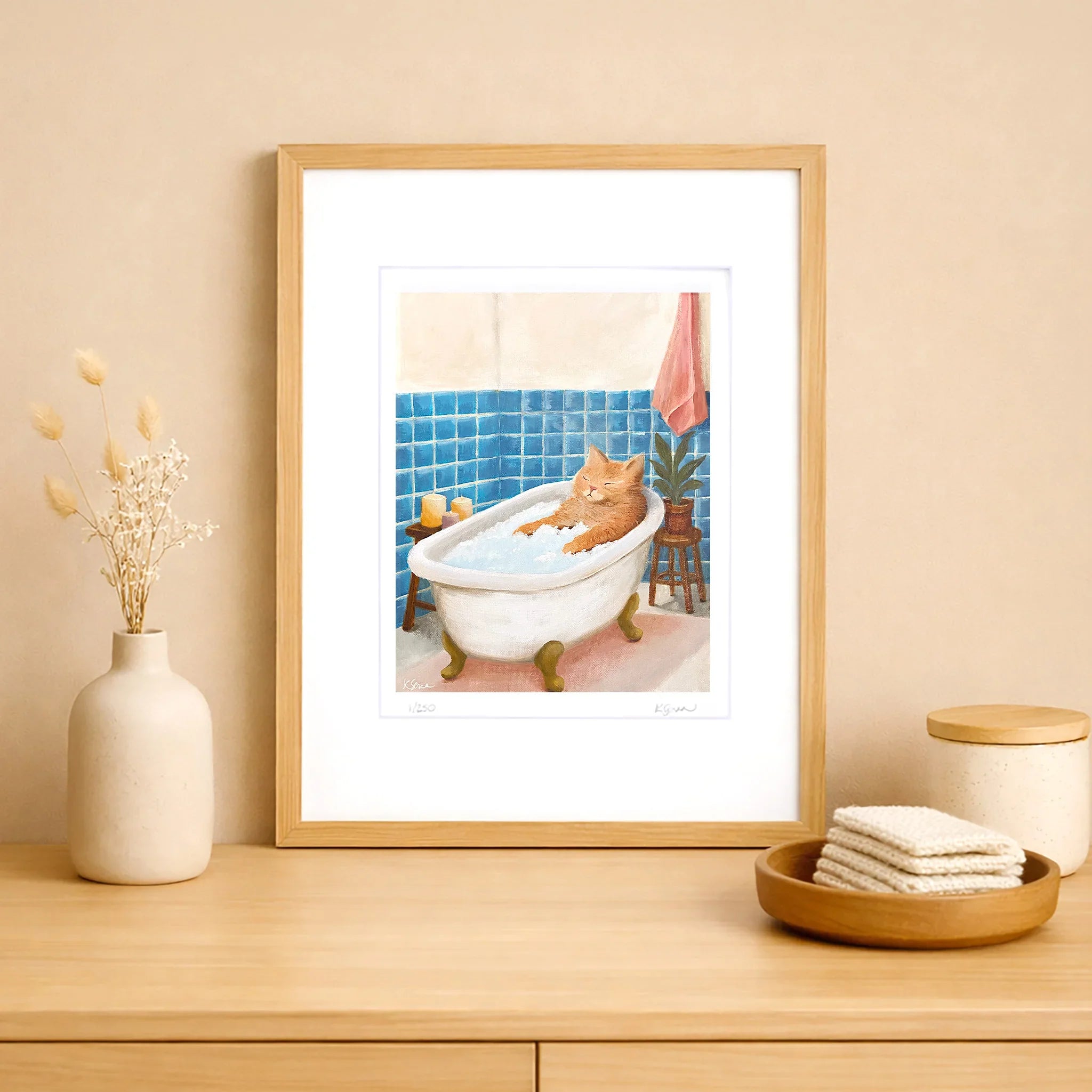 Framed artwork of a cat in a bathtub on a wooden surface with decorative items.