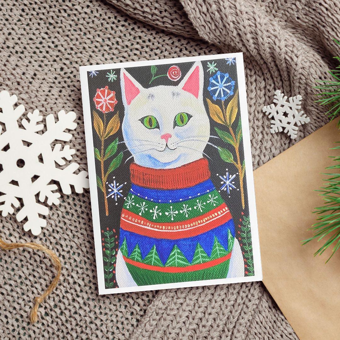 An acrylic painting of a white cat with green eyes wearing a red, blue, and green Christmas sweater against a dark background with floral and snowflake designs.