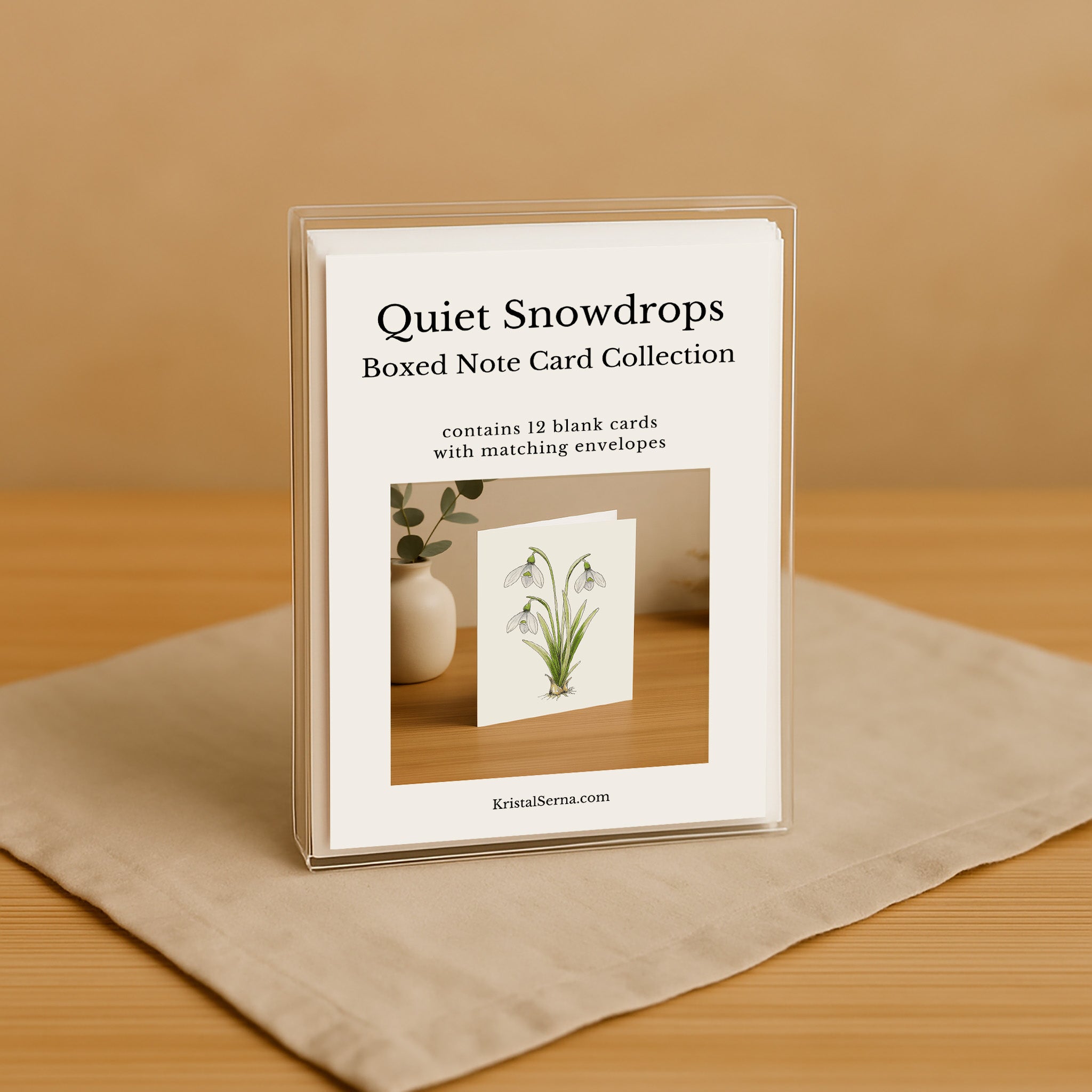 Boxed note card collection titled 'Quiet Snowdrops' on a wooden surface with a beige background.