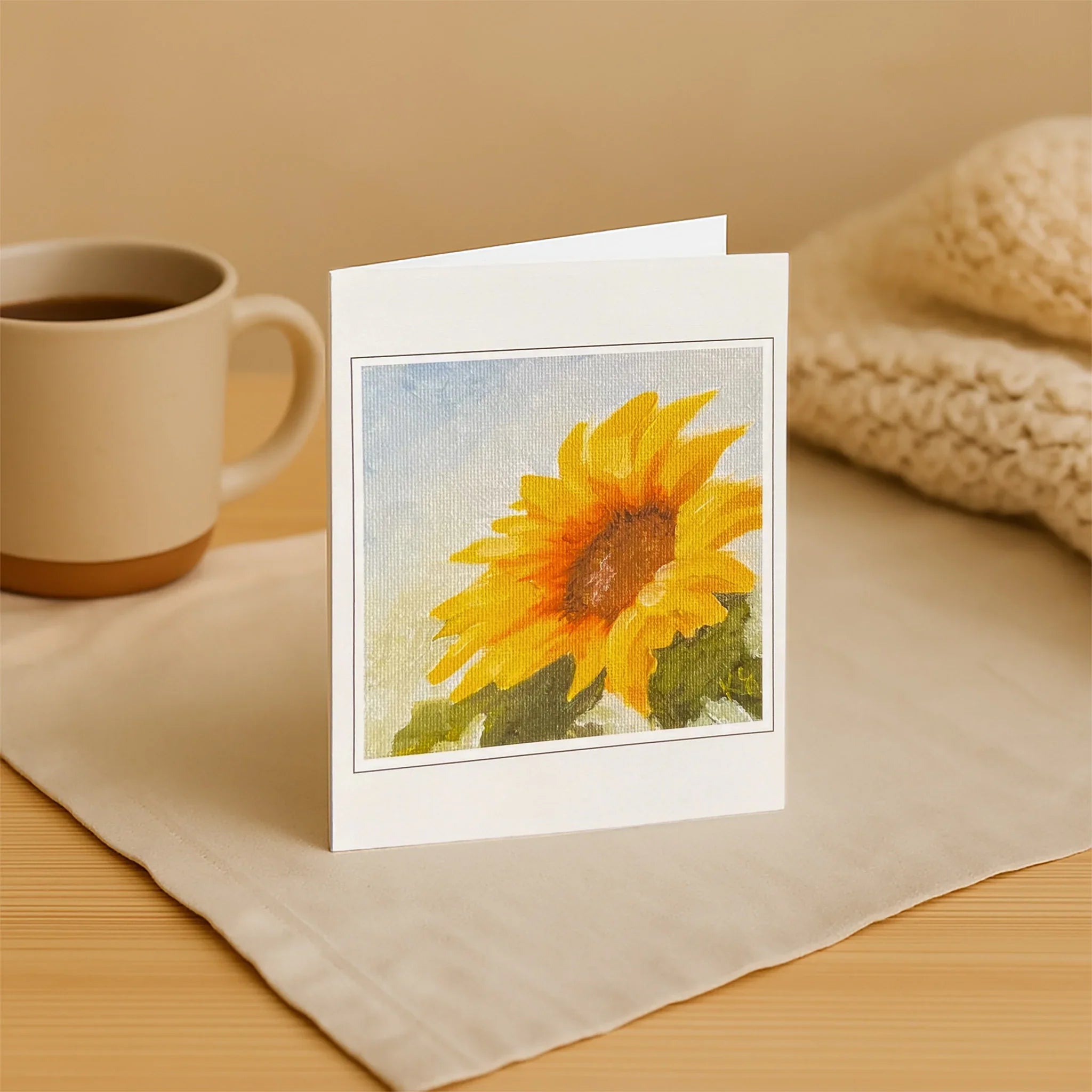 Greeting card with sunflower design on a table with a mug and fabric
