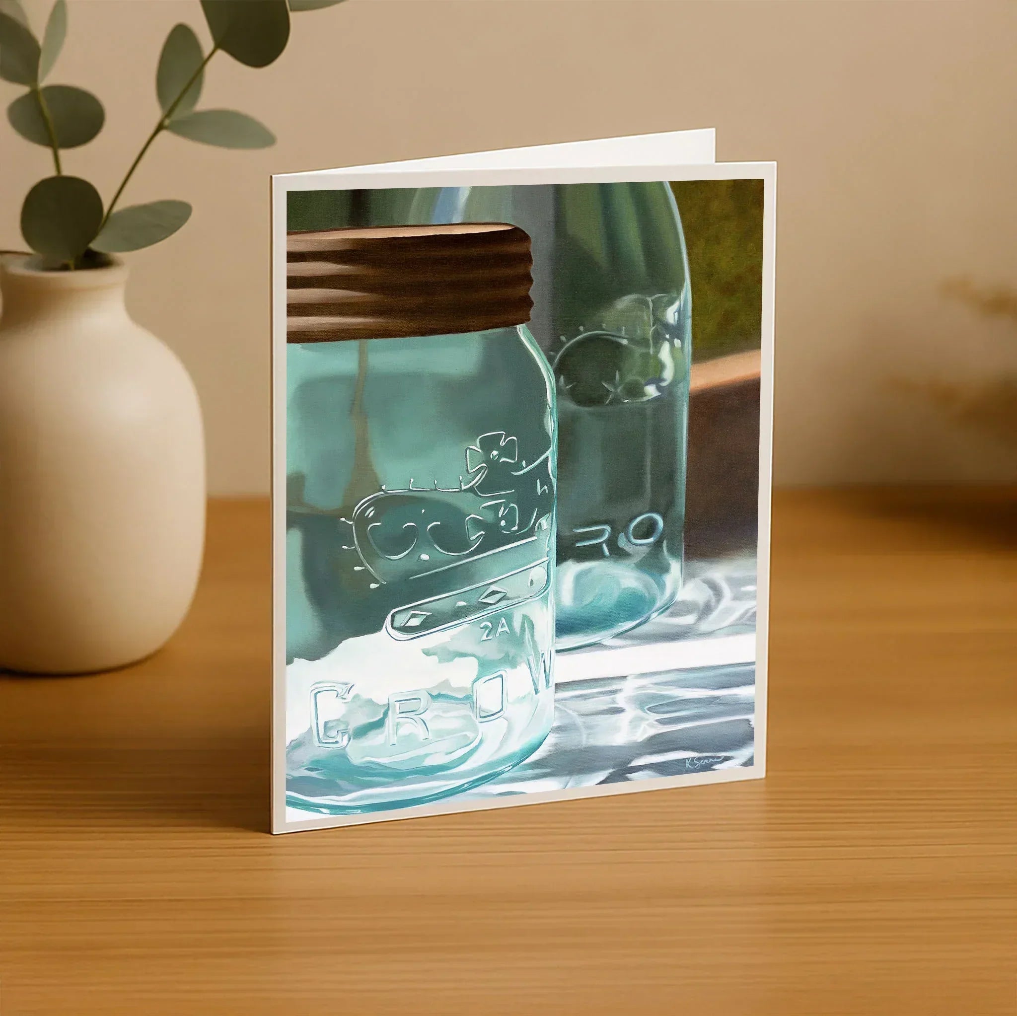 Greeting card with a mason jar design on a wooden surface with a plant in the background