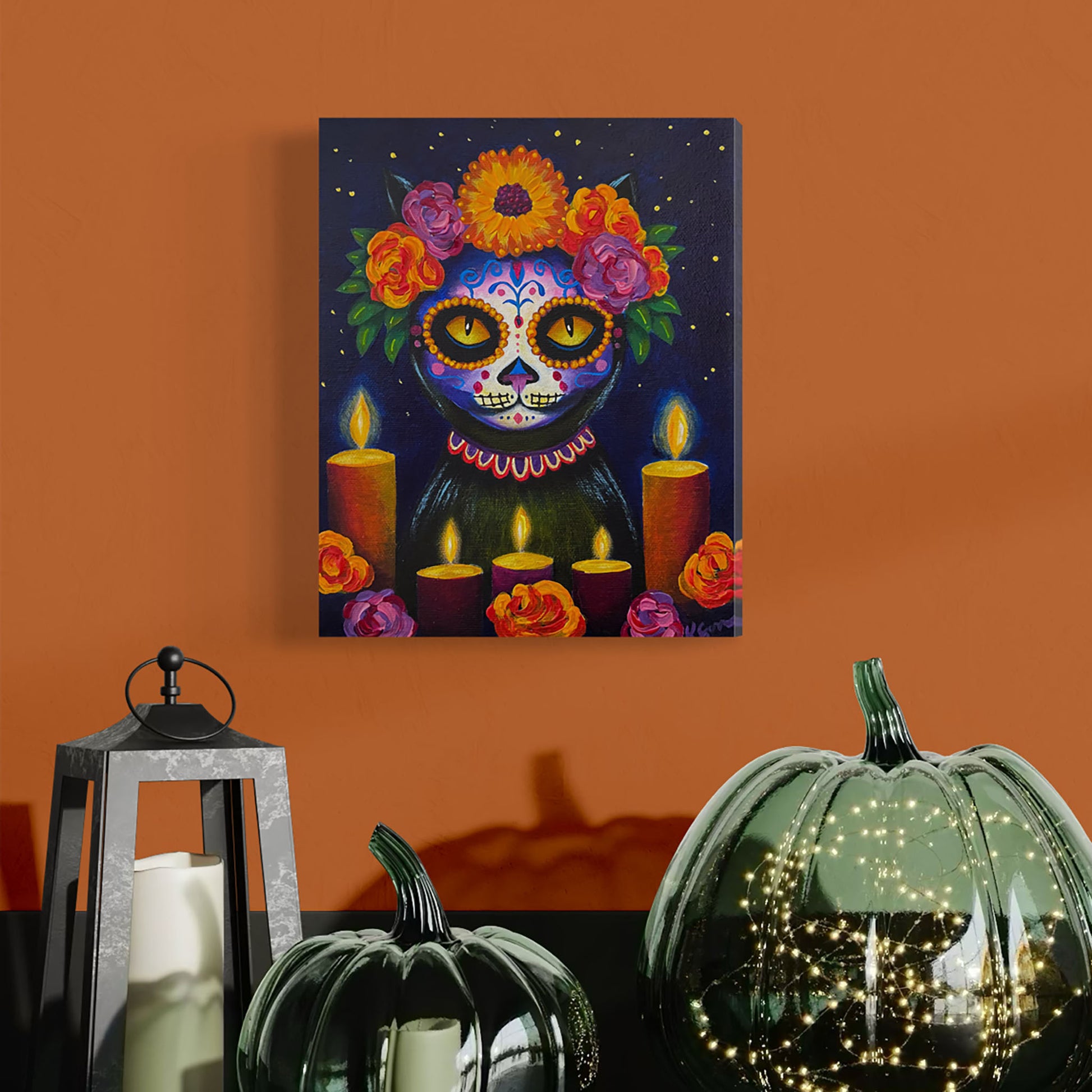 Colorful Day of the Dead-themed painting on an orange wall with pumpkins and candles.