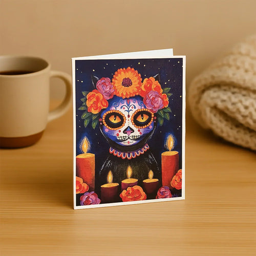 Greeting card with colorful skull design on a wooden surface with a mug and blanket in the background.