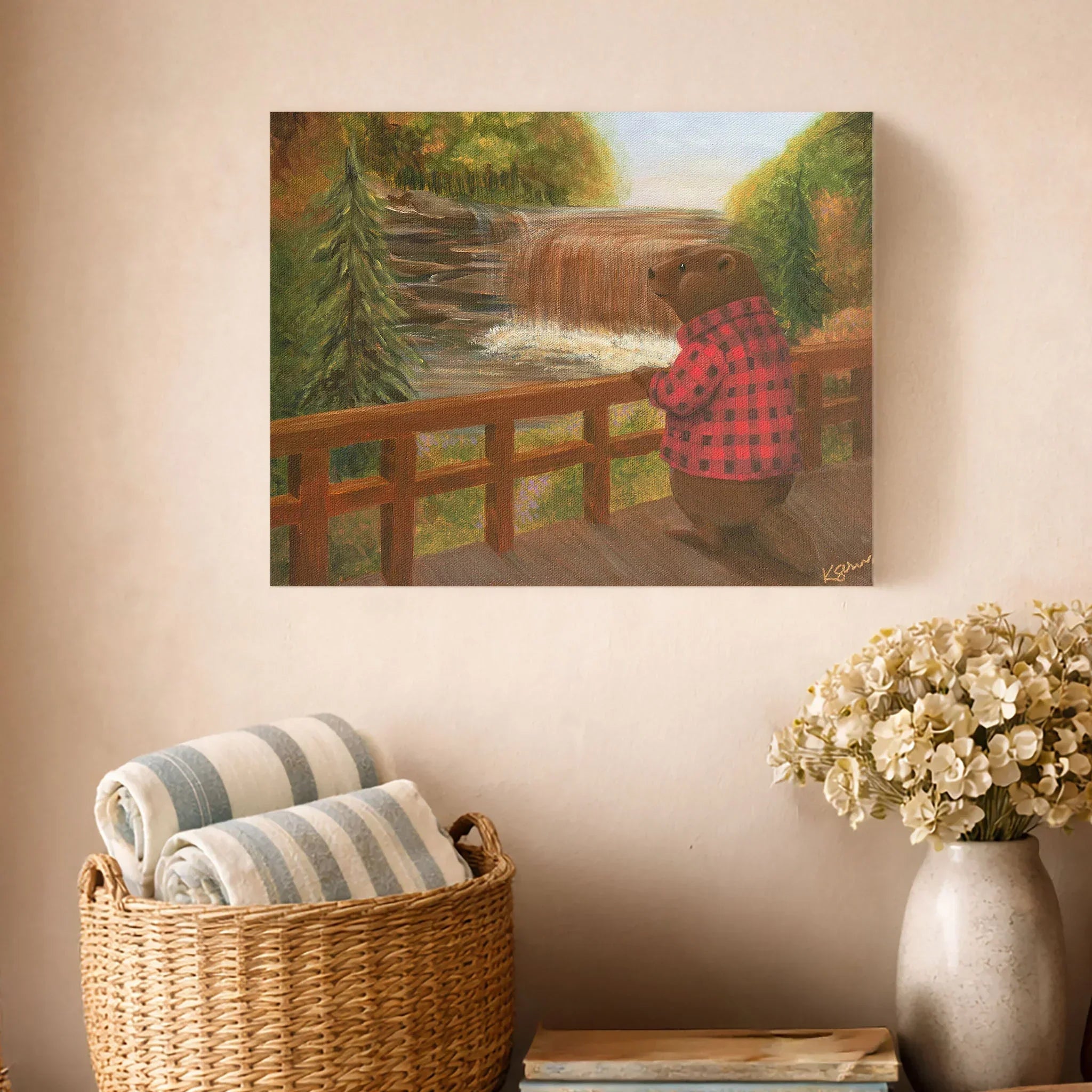 Painting of a beaver on a wooden bridge over a stream, hanging on a wall above a basket with striped towels and a vase with flowers.