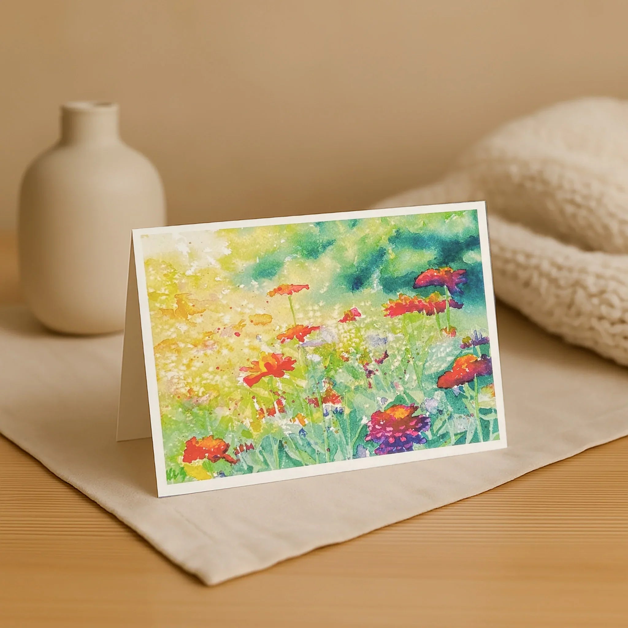 Colorful floral card on a beige surface with a vase and fabric in the background