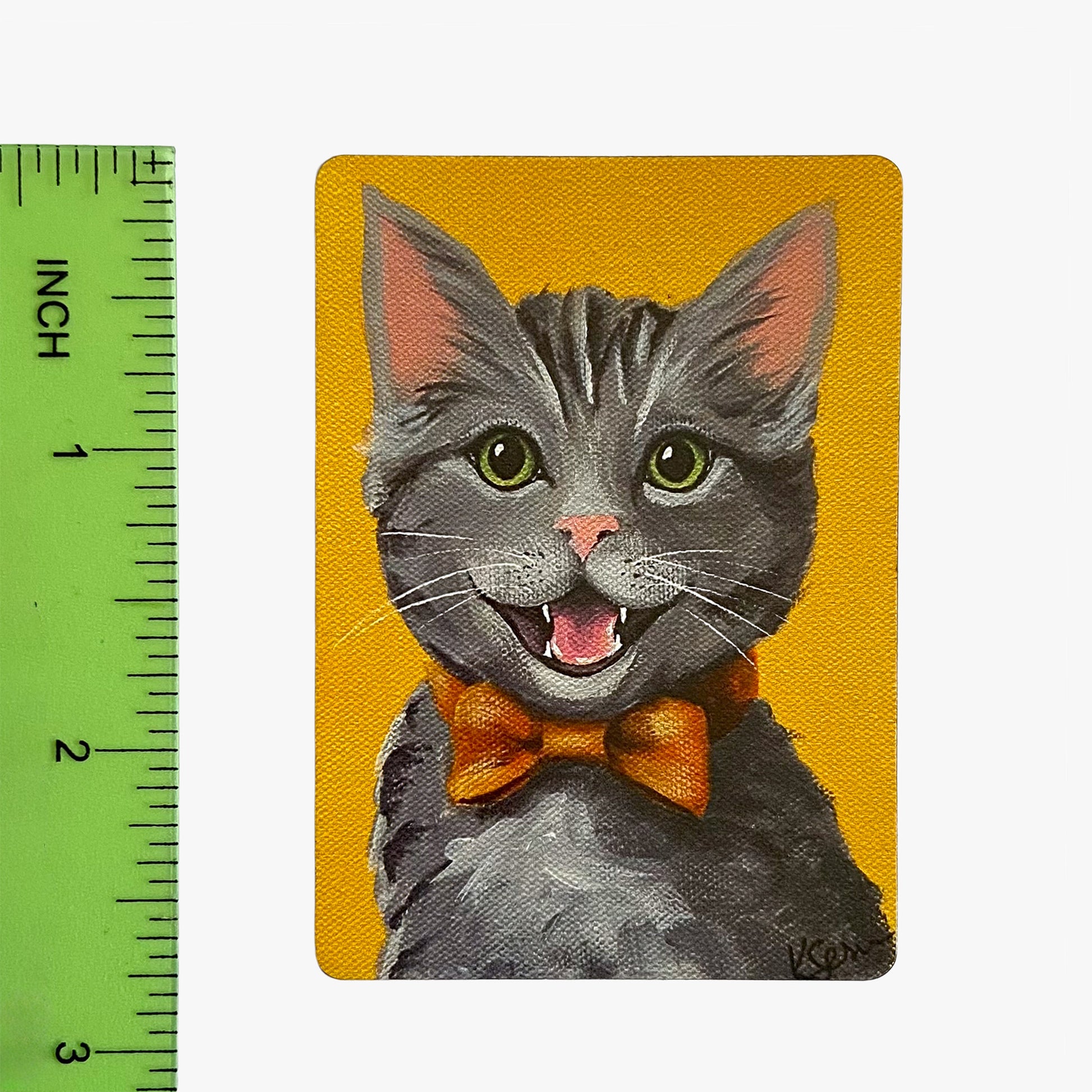Magnet with a cartoon cat wearing a bow tie on a yellow background, next to a ruler for scale.